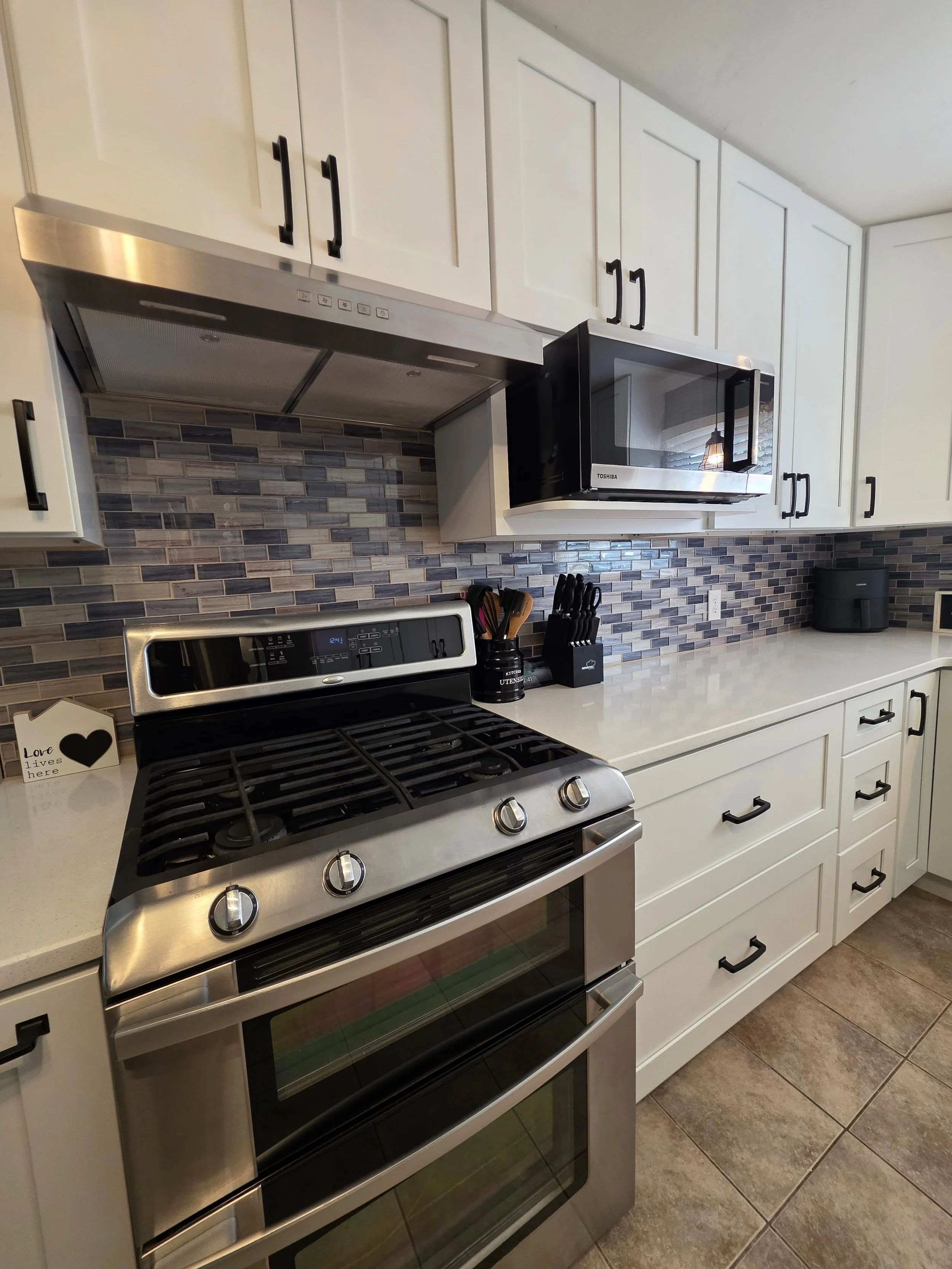Stainless range and microwave with multicolor tile backsplash.