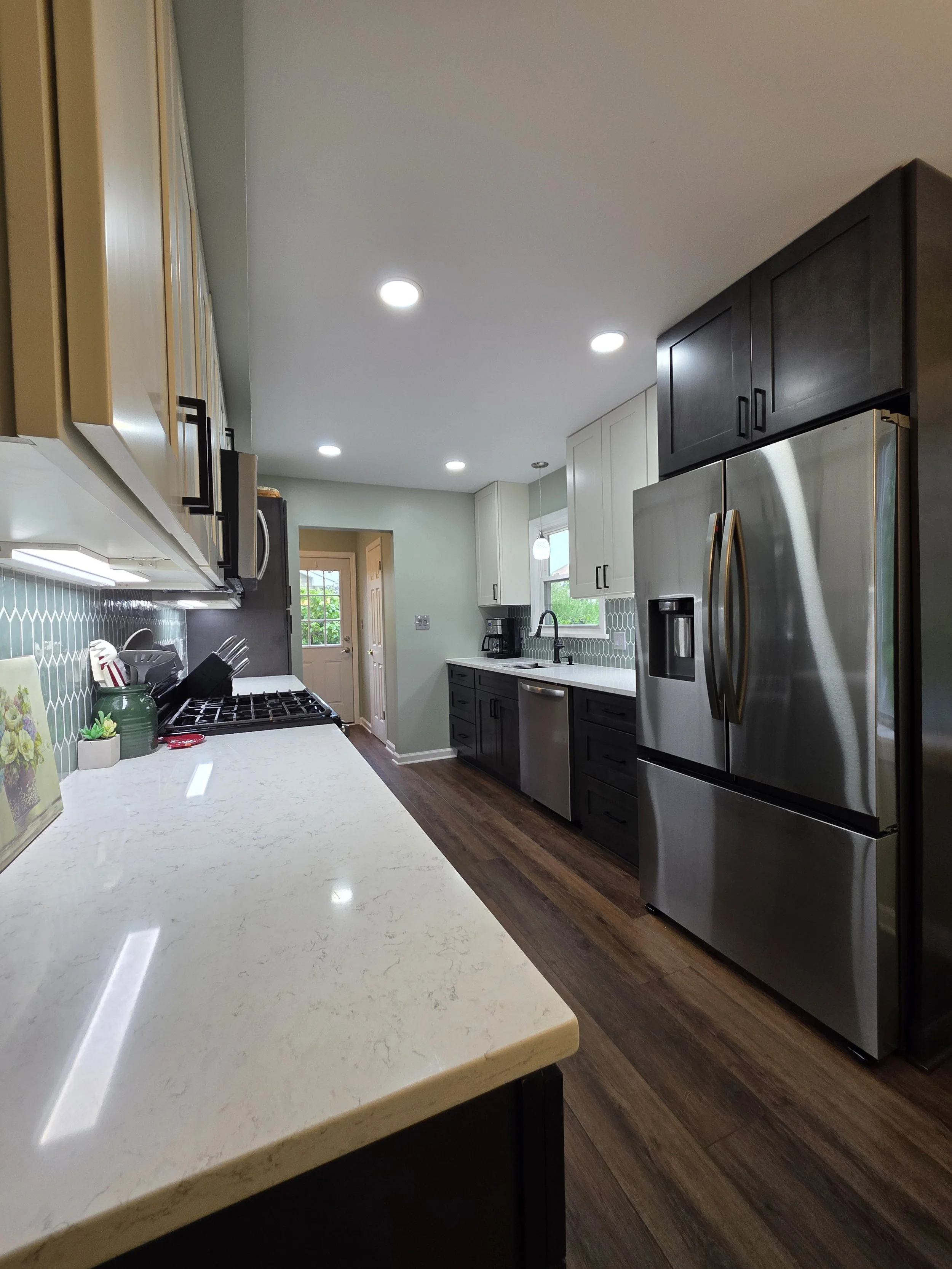 View along the kitchen counter toward the stainless refrigerator and sink area.