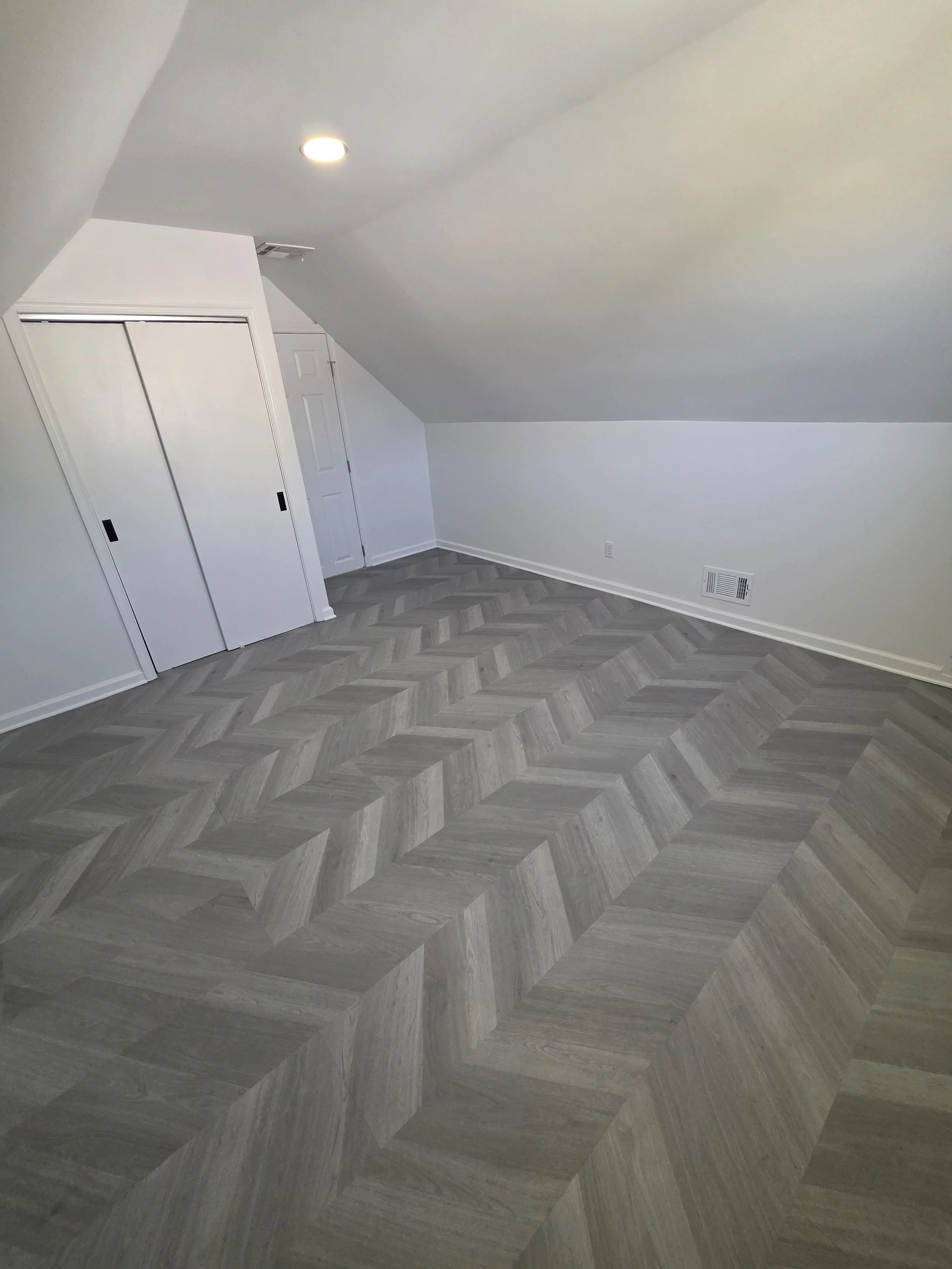 Sloped-ceiling room with white closet doors and herringbone-pattern flooring.