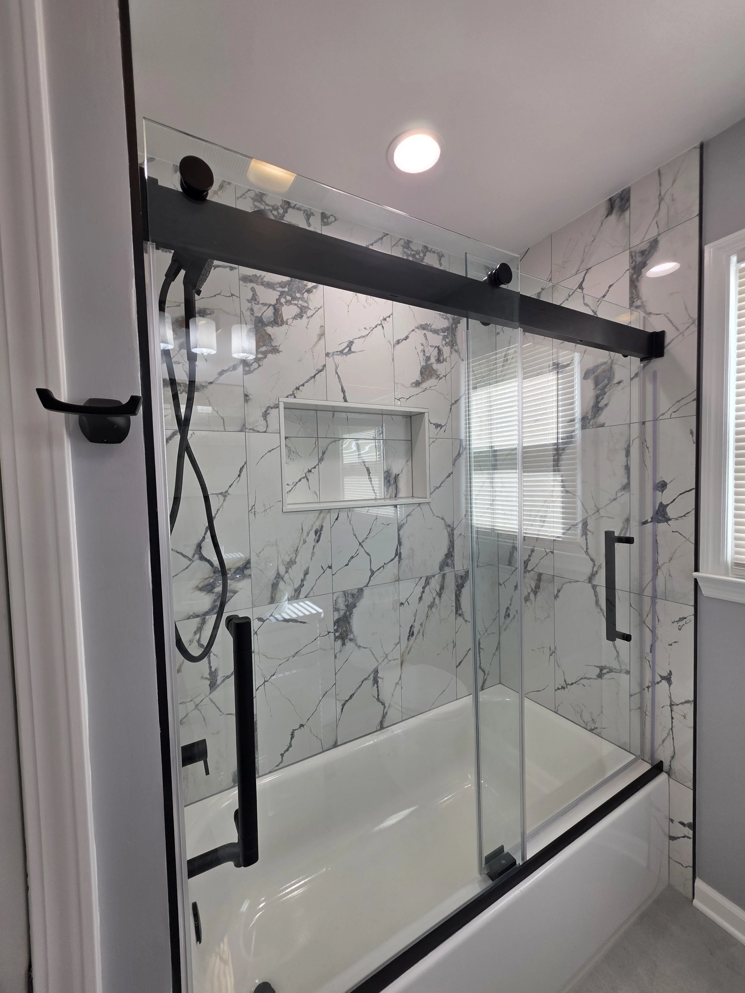 Glass tub enclosure with black sliding-door hardware and a wide recessed niche.
