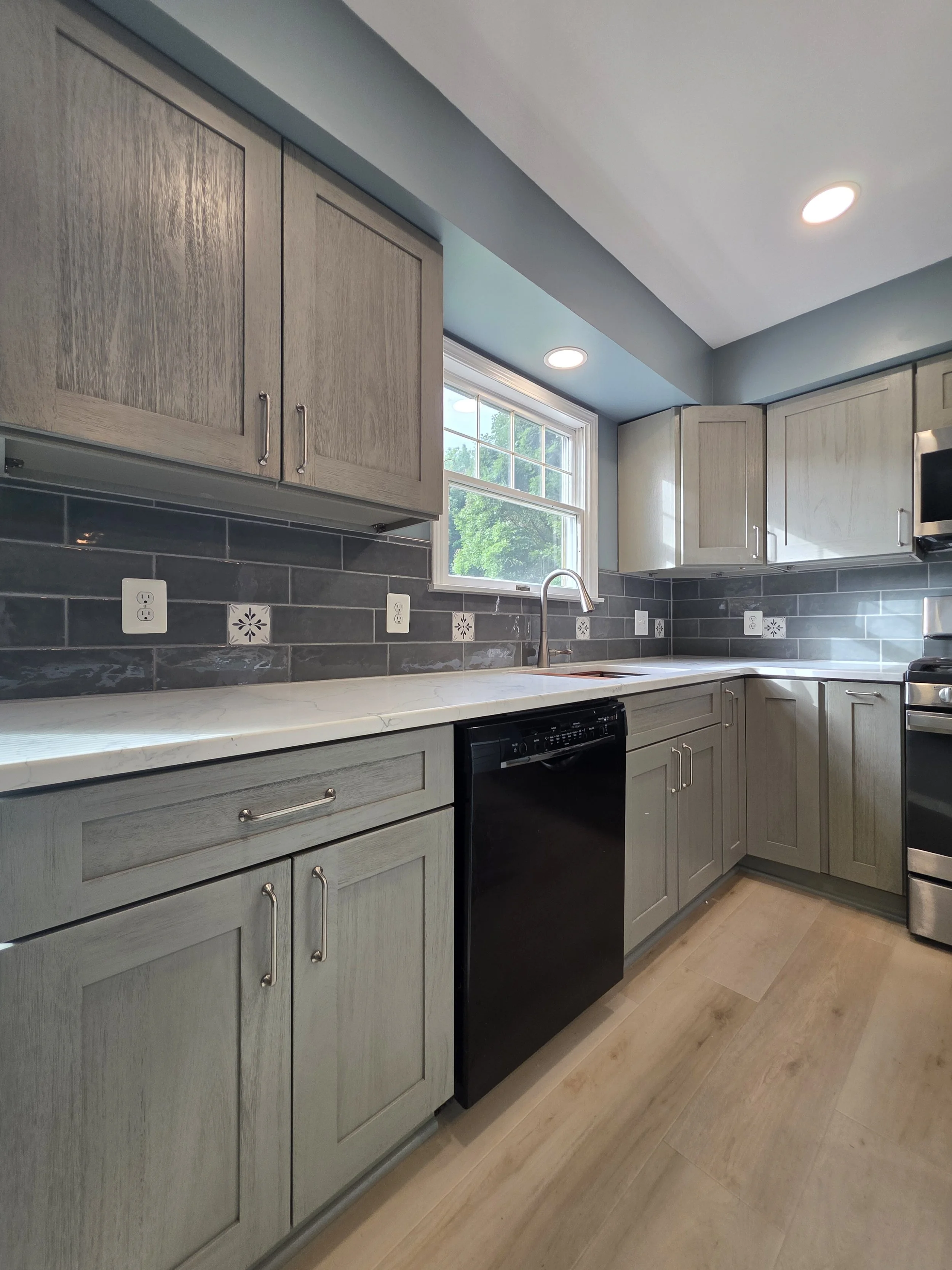 Kitchen sink below window with gray cabinetry.