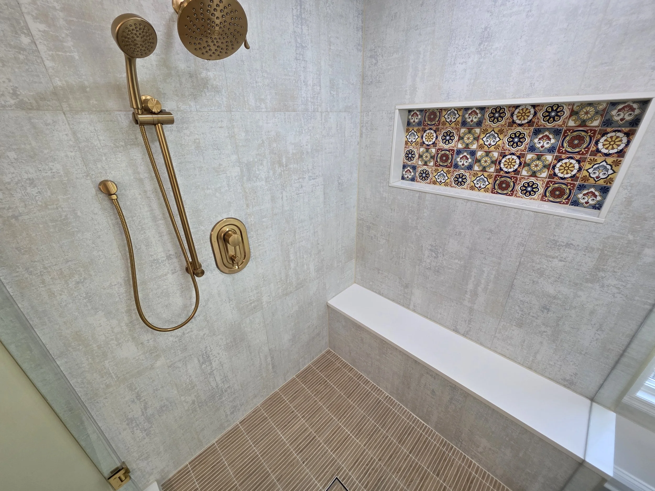 Shower interior showing the tiled bench, handheld shower, patterned niche and mosaic floor.
