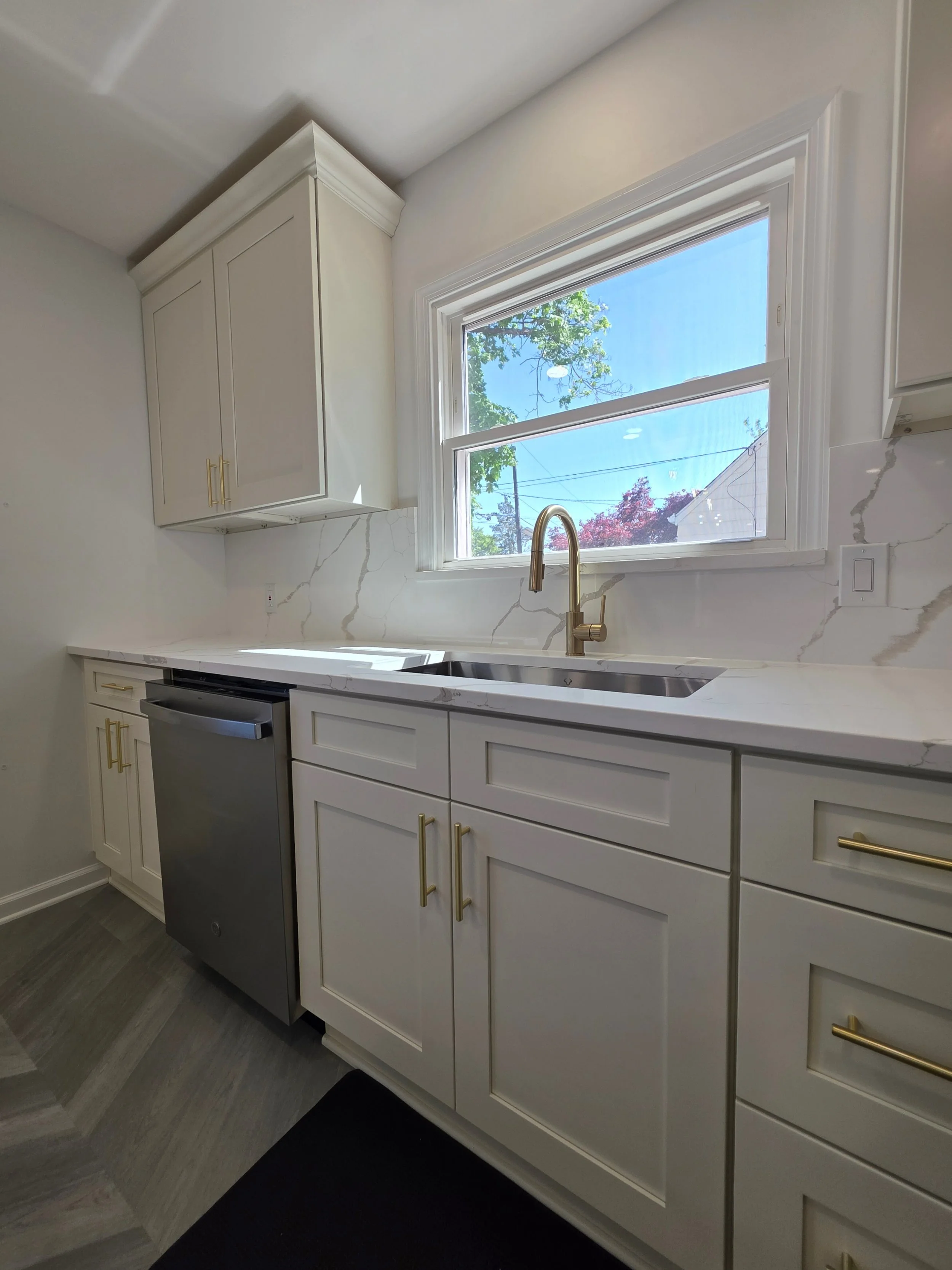 White sink cabinetry with gold-tone handles beside the stainless dishwasher.