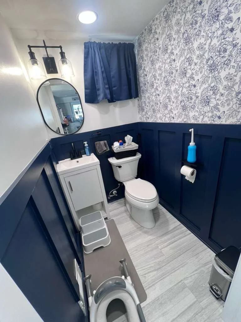 Before renovation: the original first-floor bathroom with dark blue wall paneling, patterned wallpaper and a small vanity.