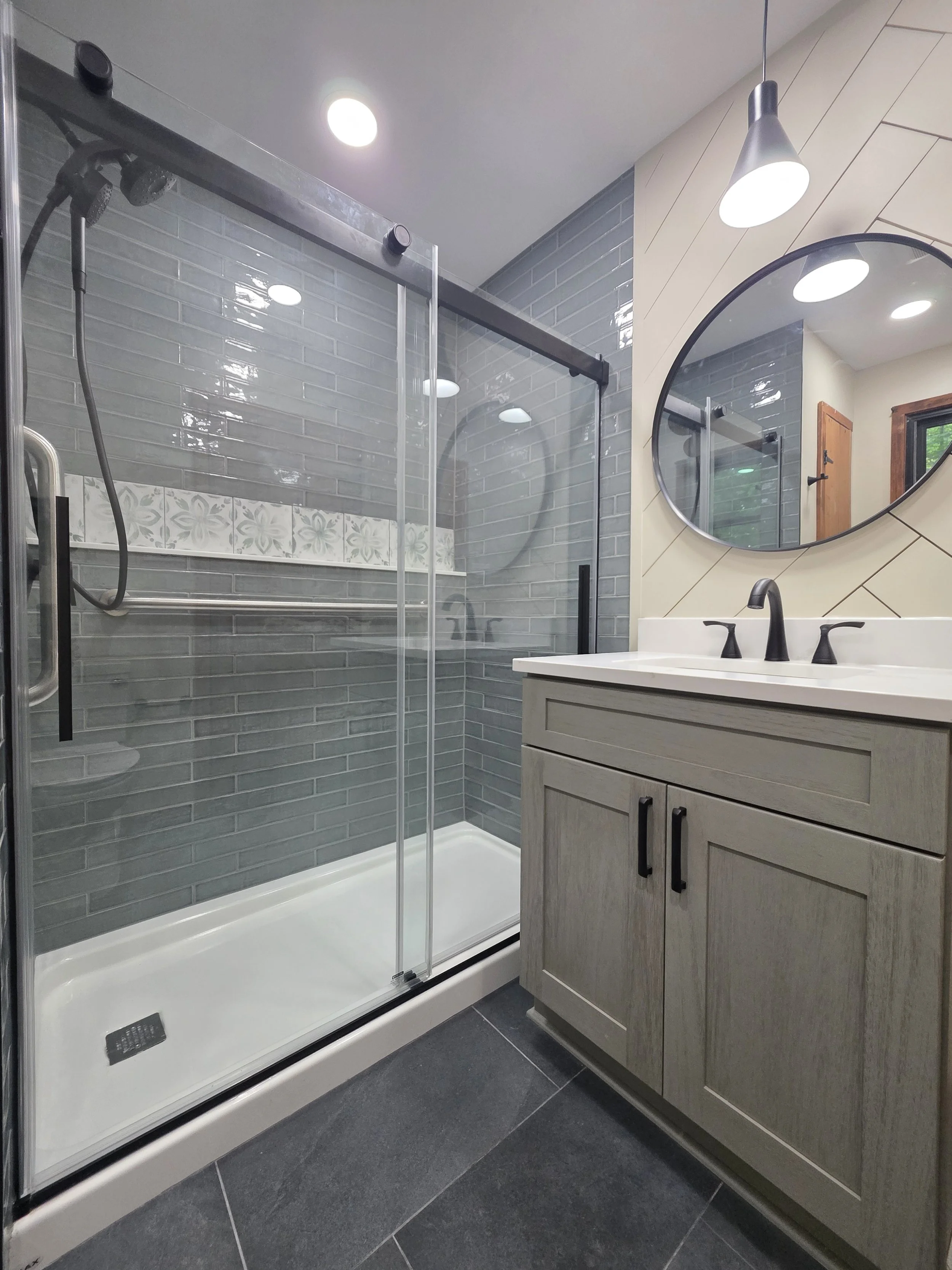 Glass shower beside the vanity, showing gray wall tile and a patterned shower ledge.