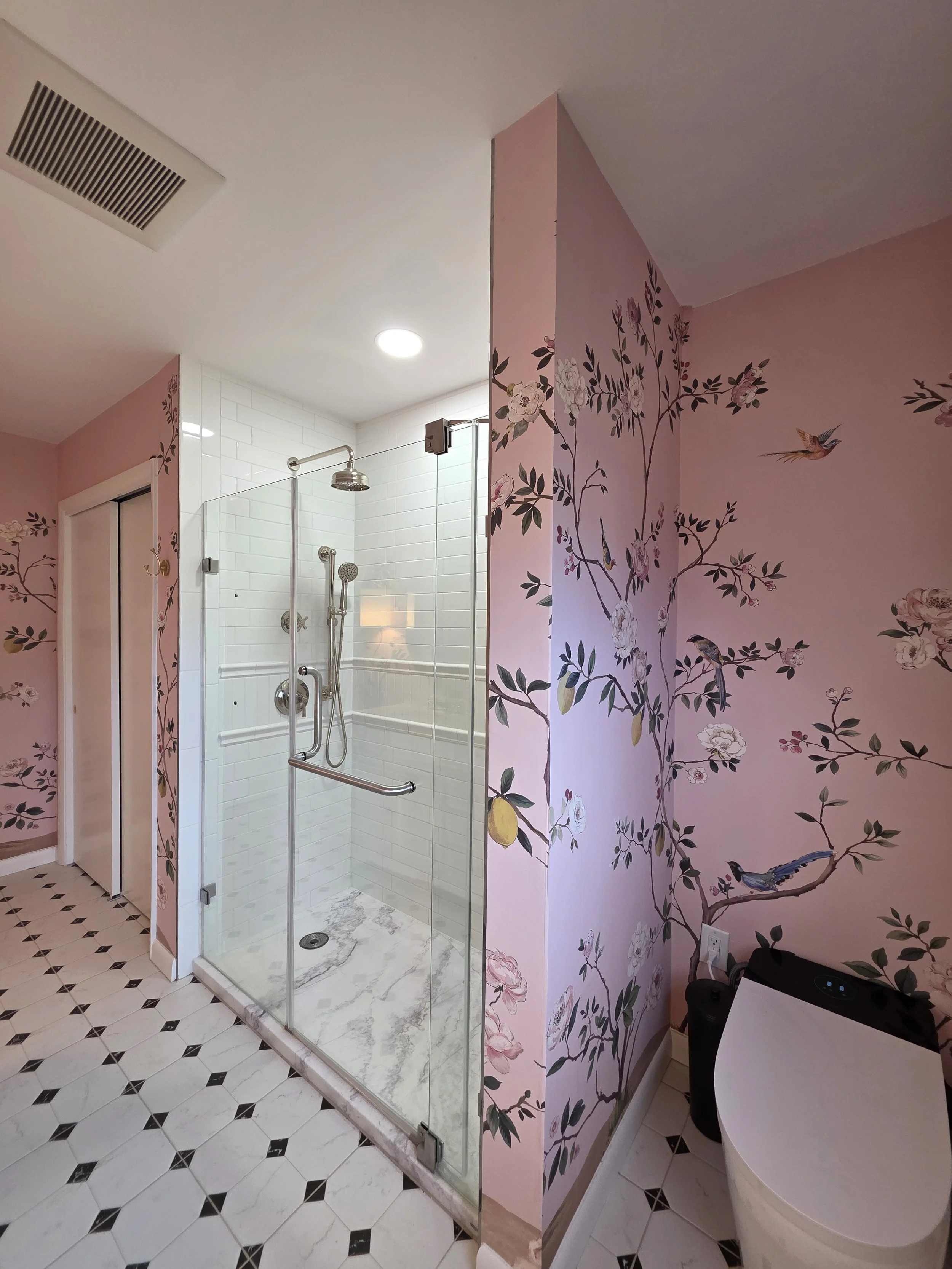 Glass shower beside pink wallpaper and toilet.