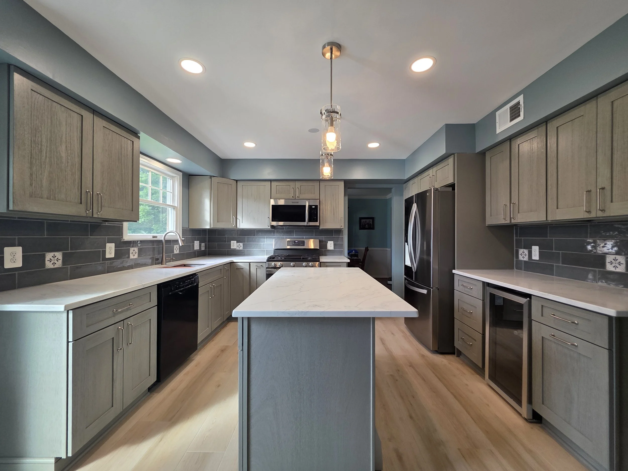 Doug and Corinne’s completed kitchen with gray cabinetry, island and light countertops.
