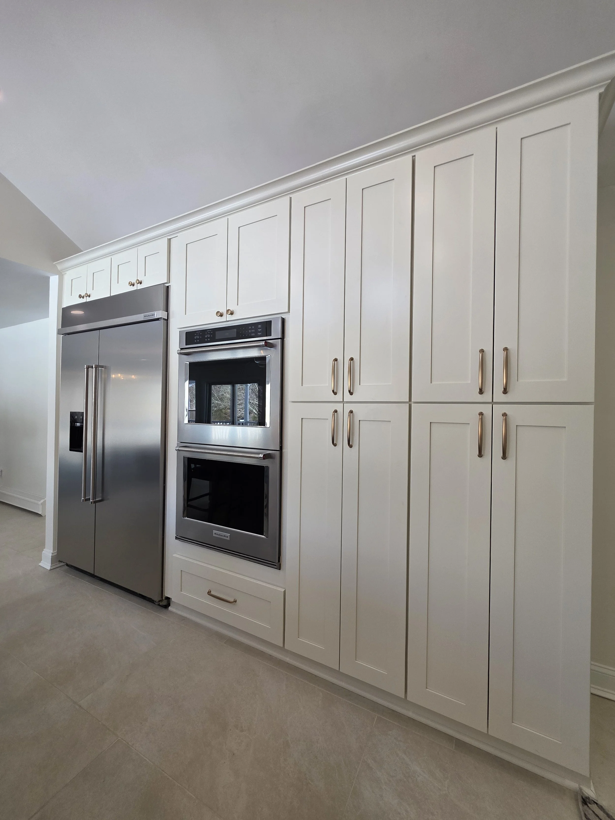 White storage cabinets surrounding the stainless refrigerator and stacked wall ovens.