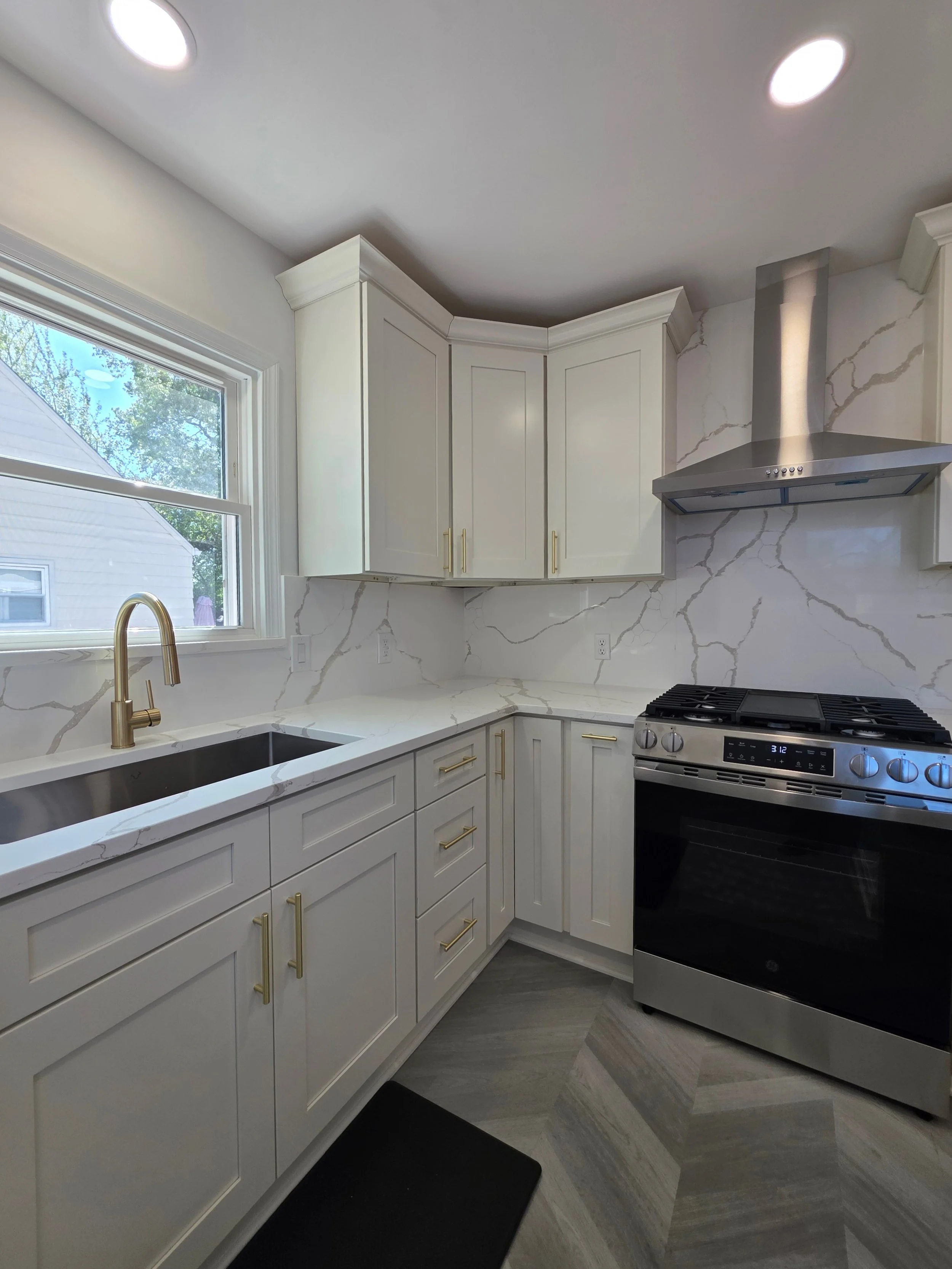 White corner cabinets and veined backsplash surrounding the sink and stainless range.