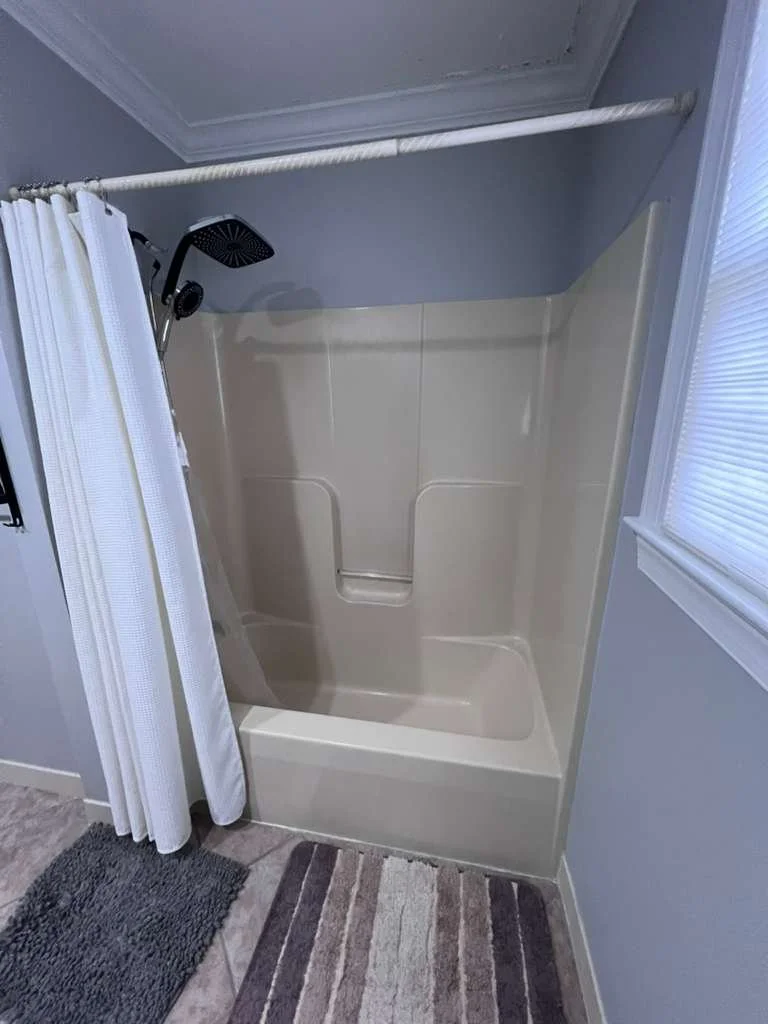 Before renovation: the original white tub surround, shower curtain and dark showerhead.