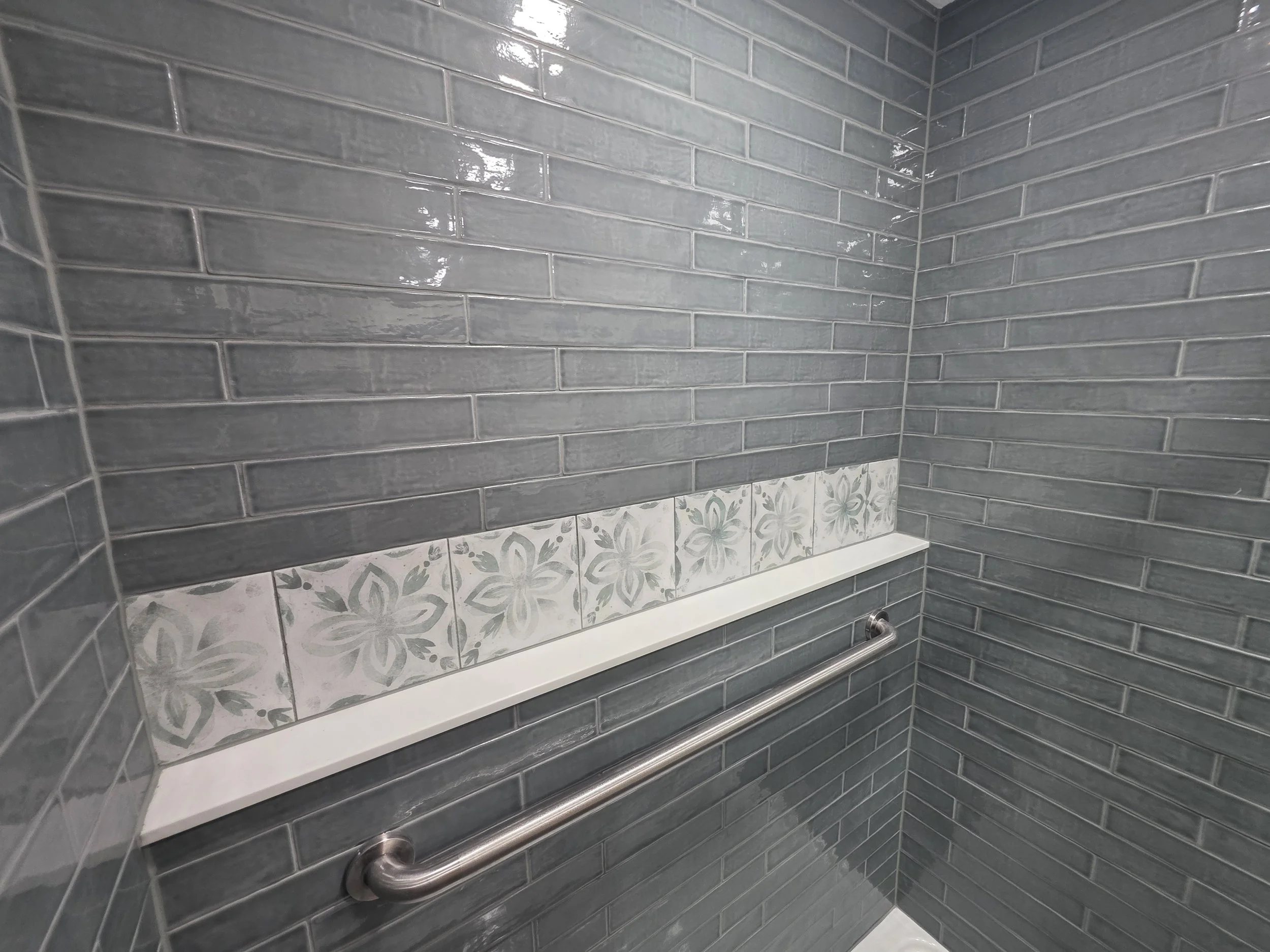 Close view of the patterned shower ledge and horizontal grab bar against gray tile.