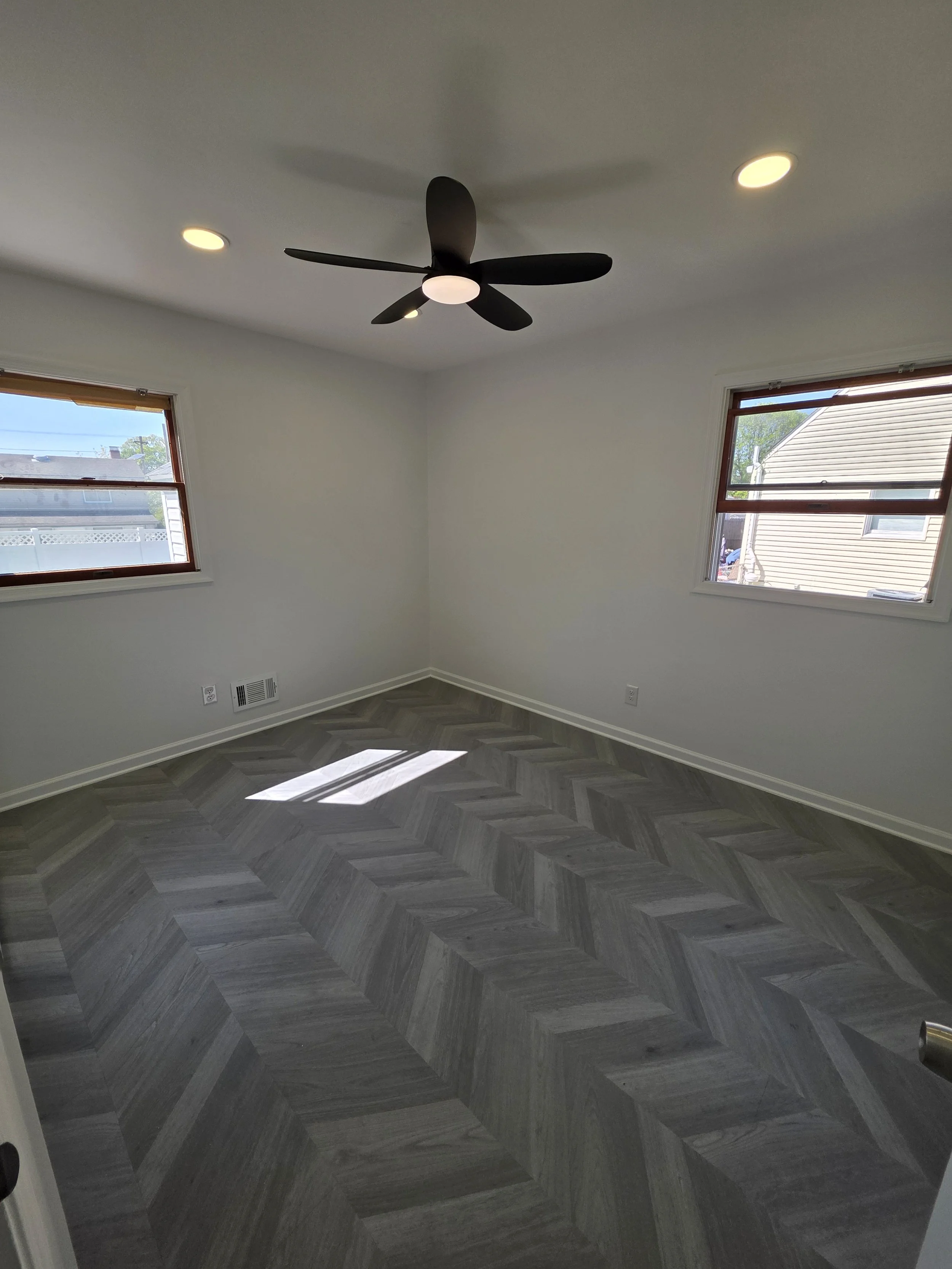 Room with a ceiling fan, recessed lights and herringbone-pattern floor.