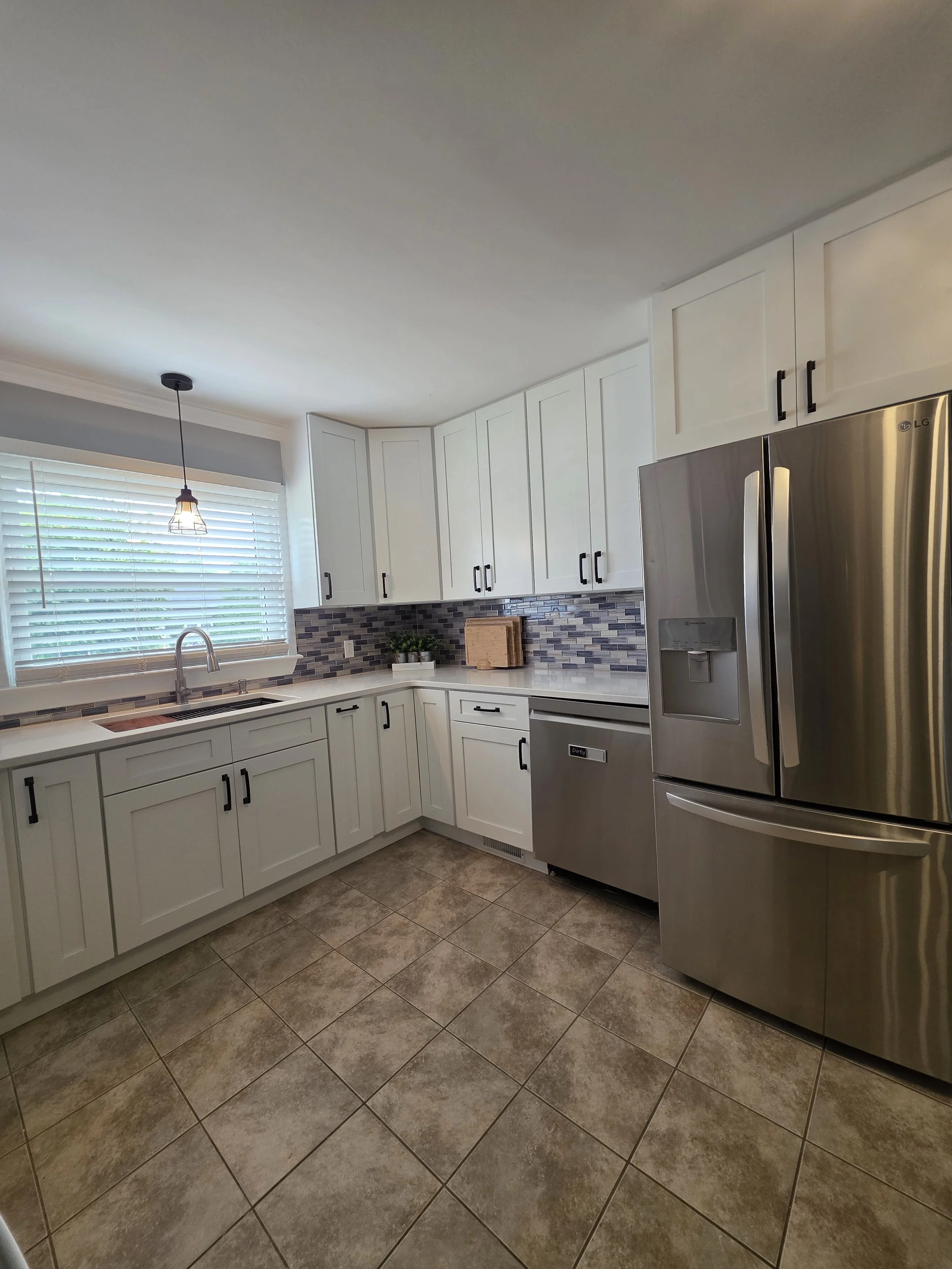 Kitchen sink and refrigerator surrounded by white cabinets.