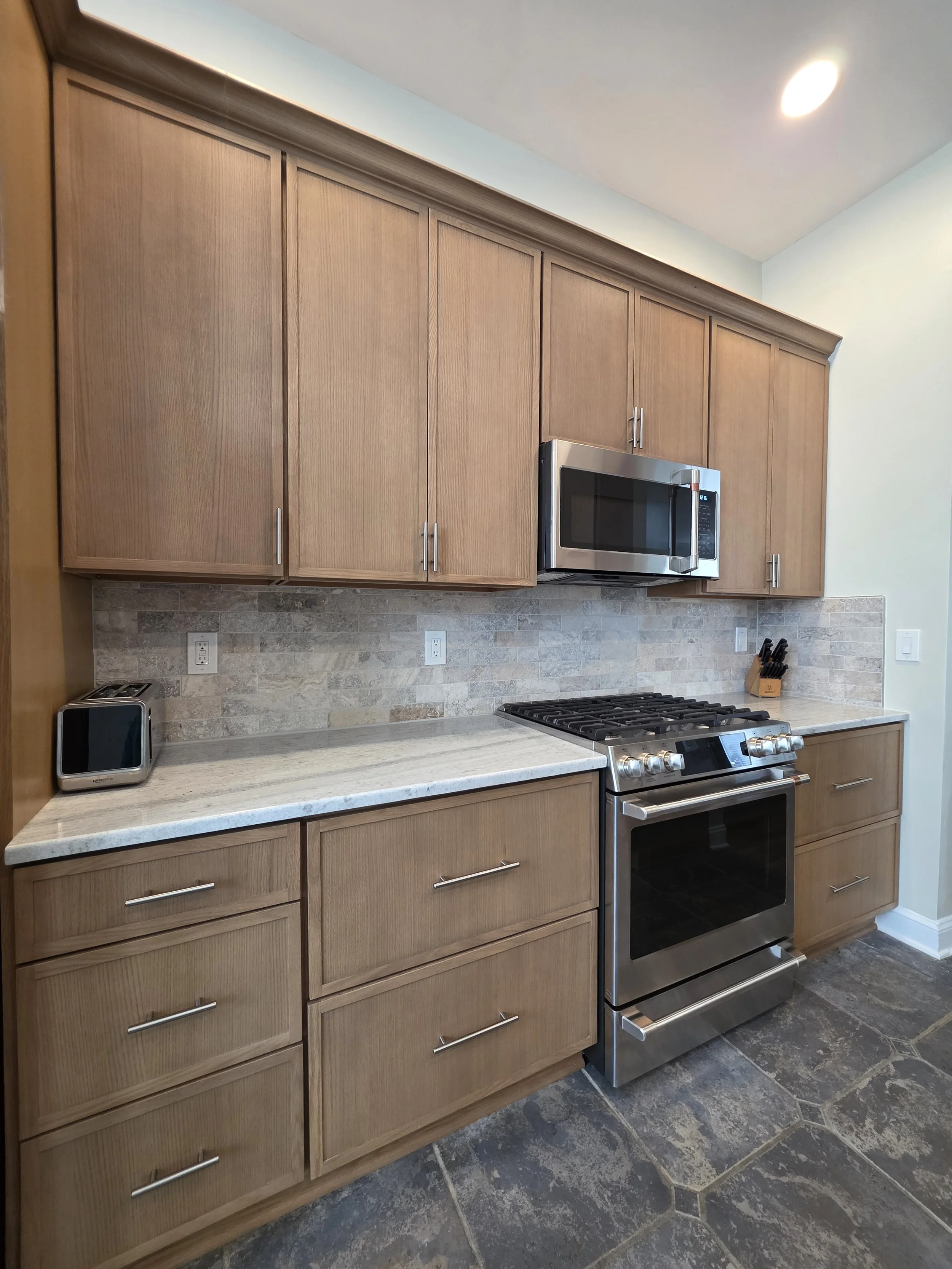 Range and microwave surrounded by wood cabinetry and a tiled backsplash.