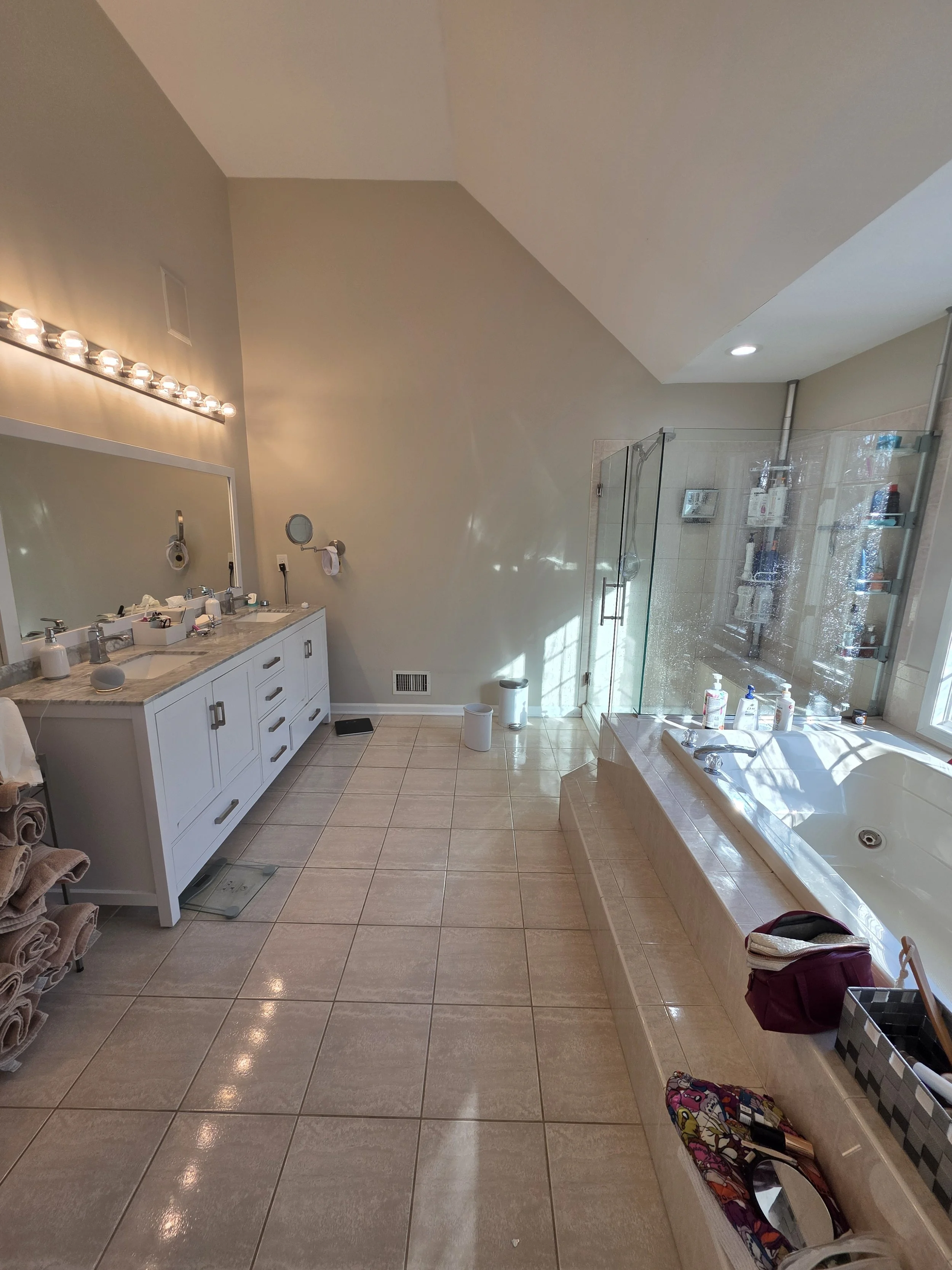 Before renovation: the original master bathroom with a built-in tub, white vanity and square floor tiles.