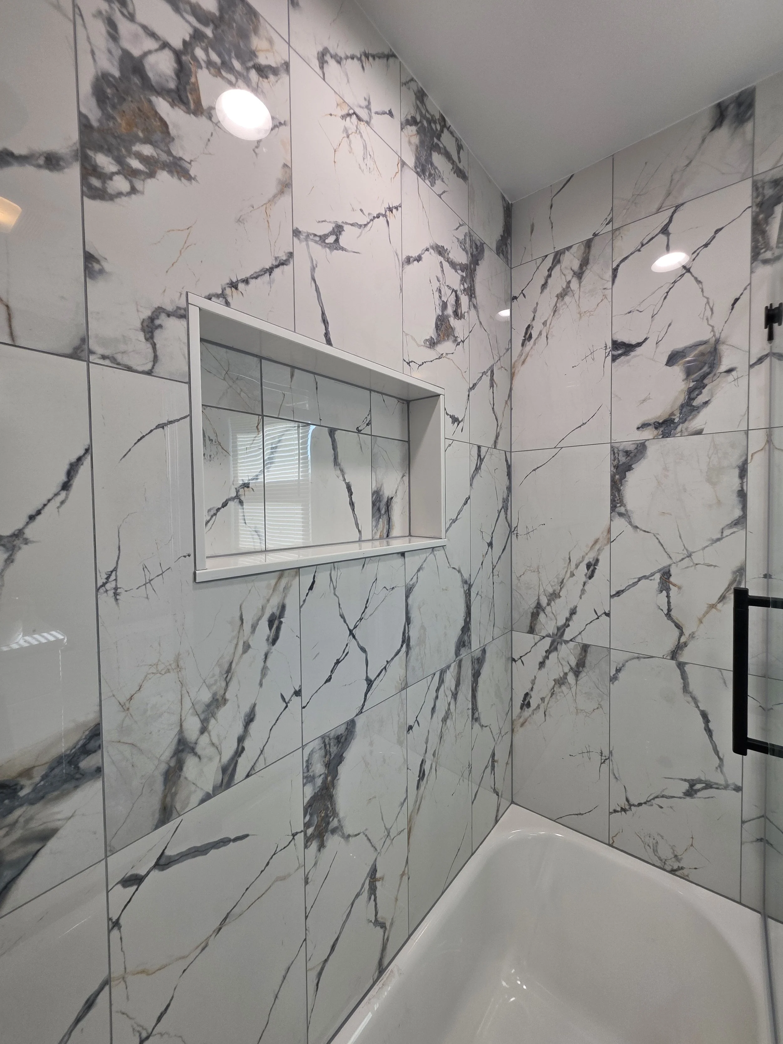 Angled view of the white bathtub and veined wall tile around the recessed niche.