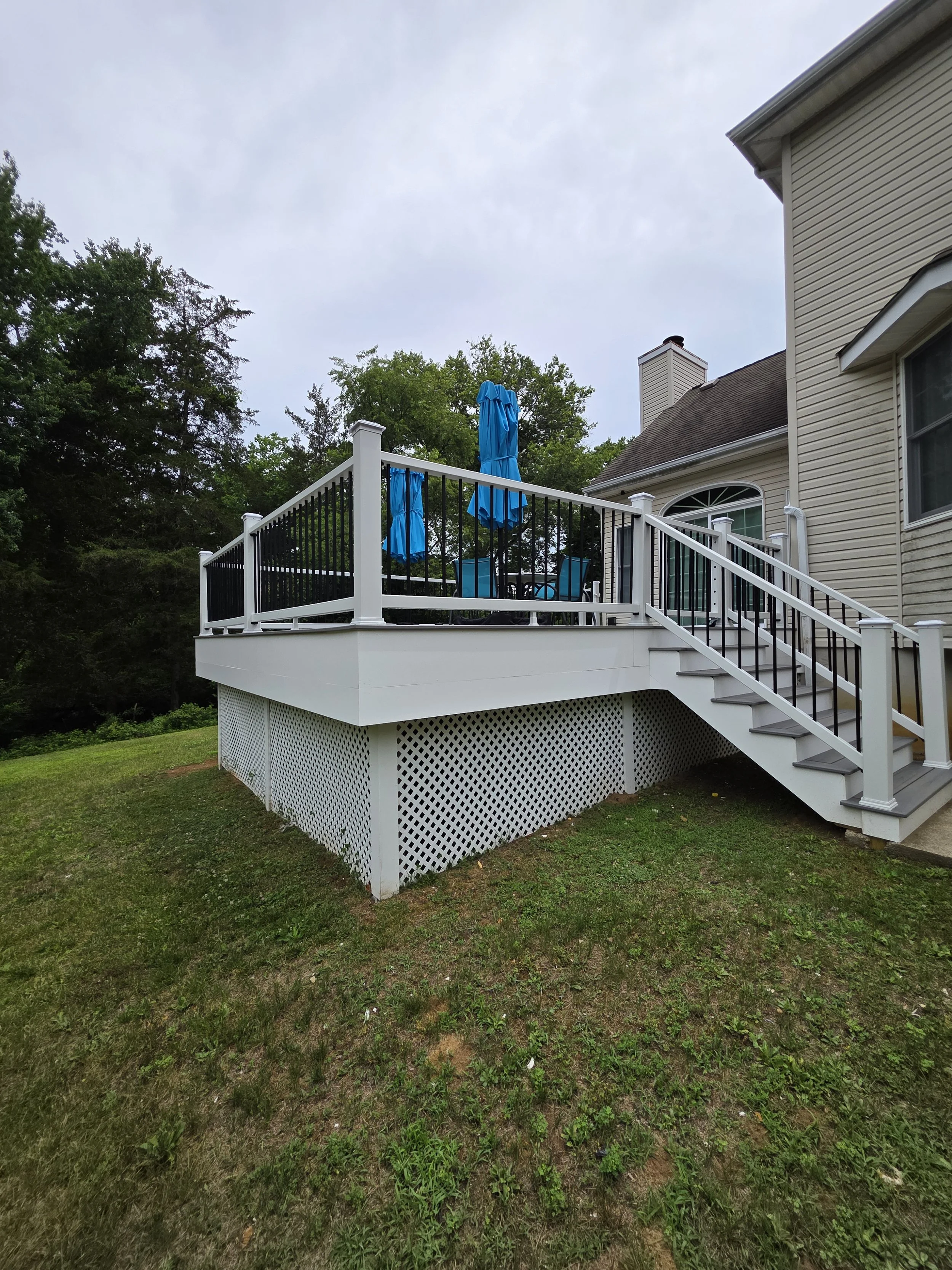 Completed attached house deck with gray decking, white railings, black balusters, and side stairs.
