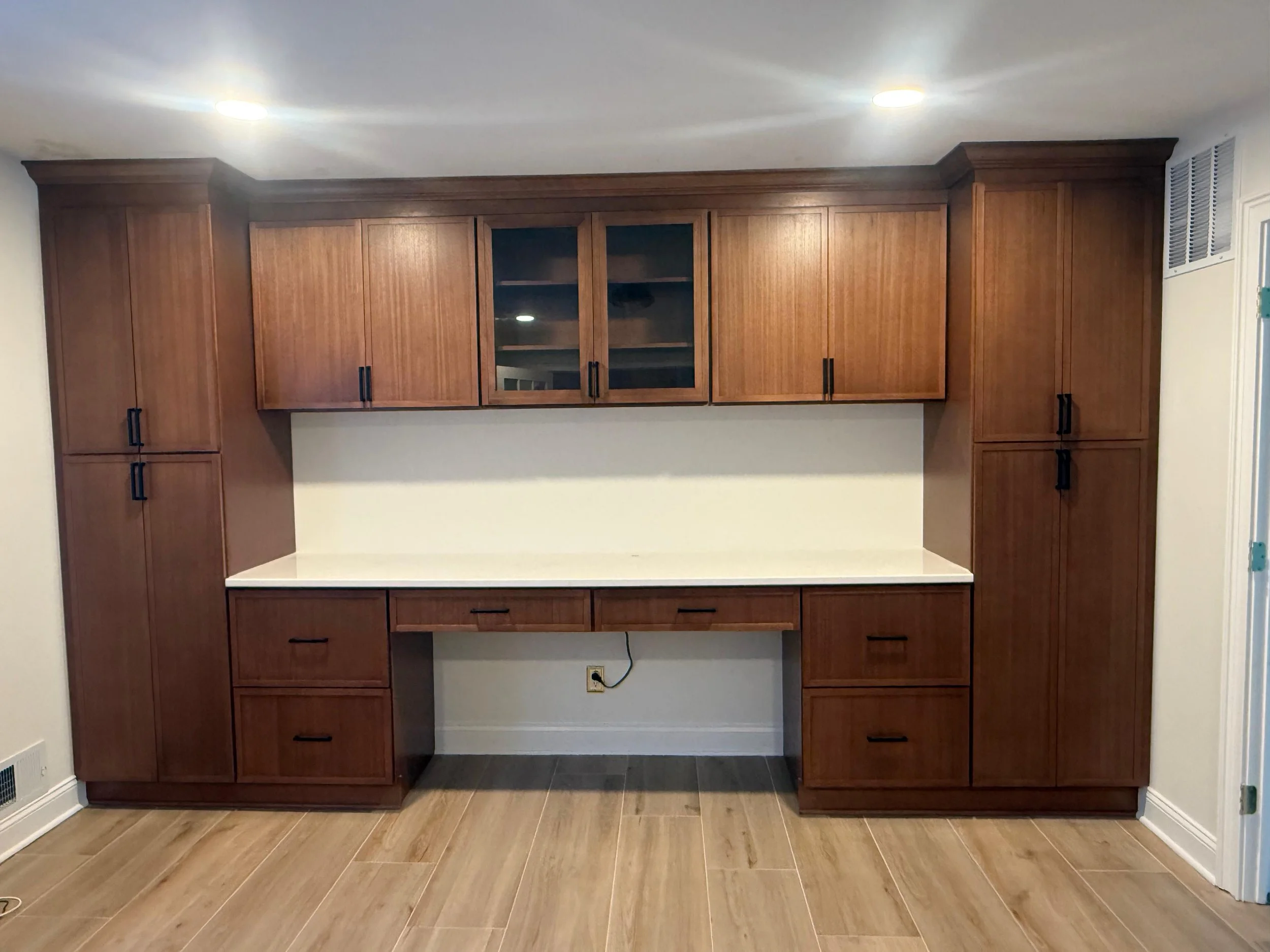 Second view of the built-in office desk framed by tall storage cabinets and upper wood cabinetry.