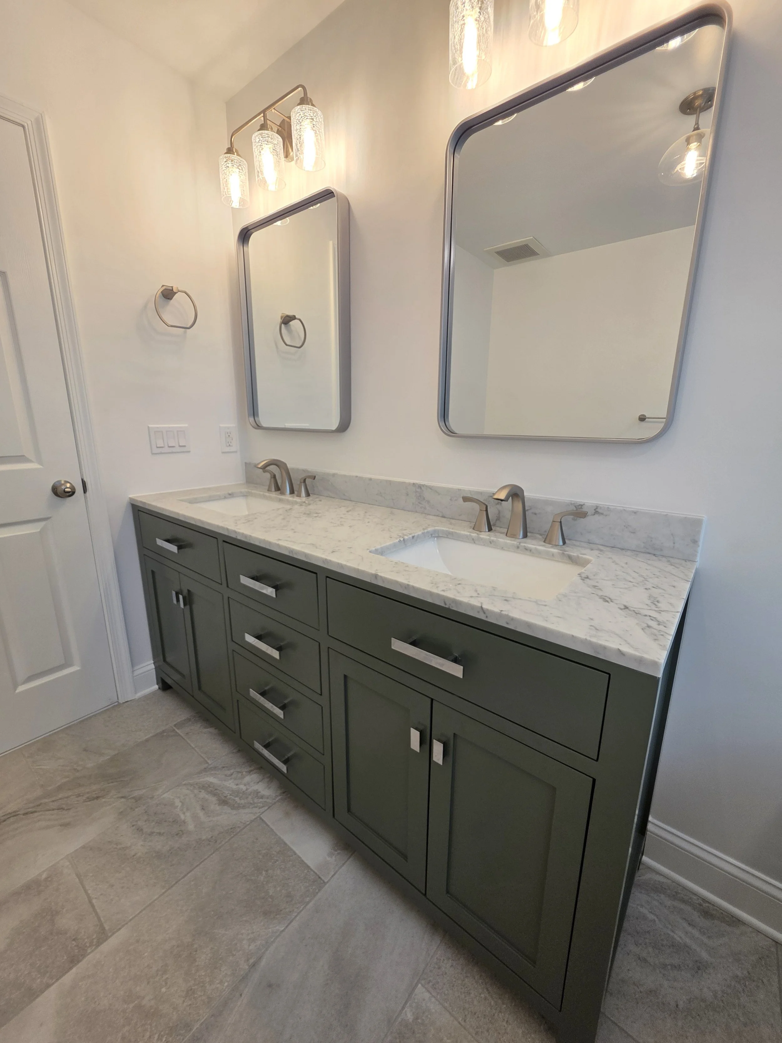 Green double vanity with a light countertop, two rectangular mirrors and overhead vanity lights.
