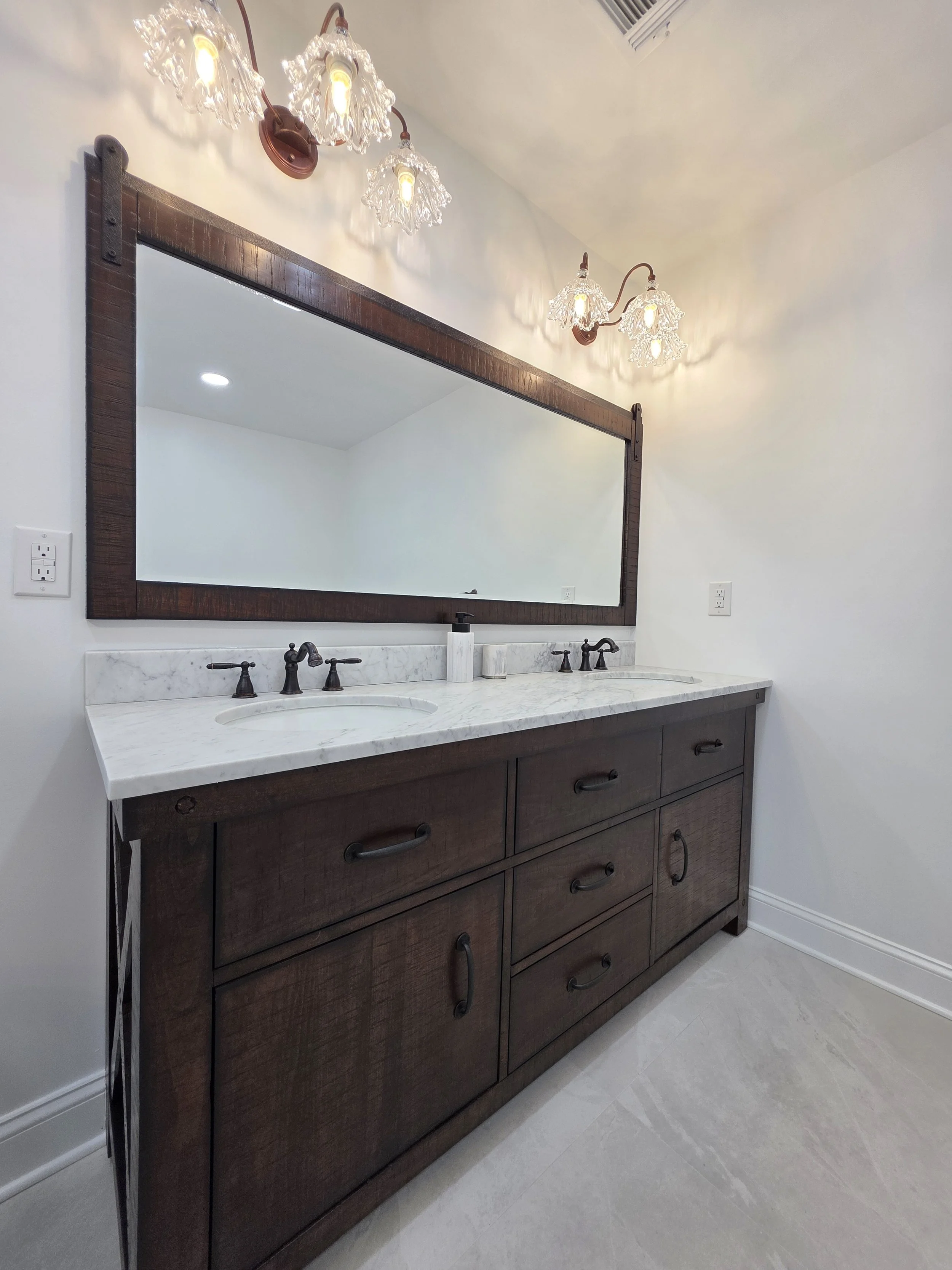 Dark double vanity with white countertop, black faucets and a wide framed mirror.