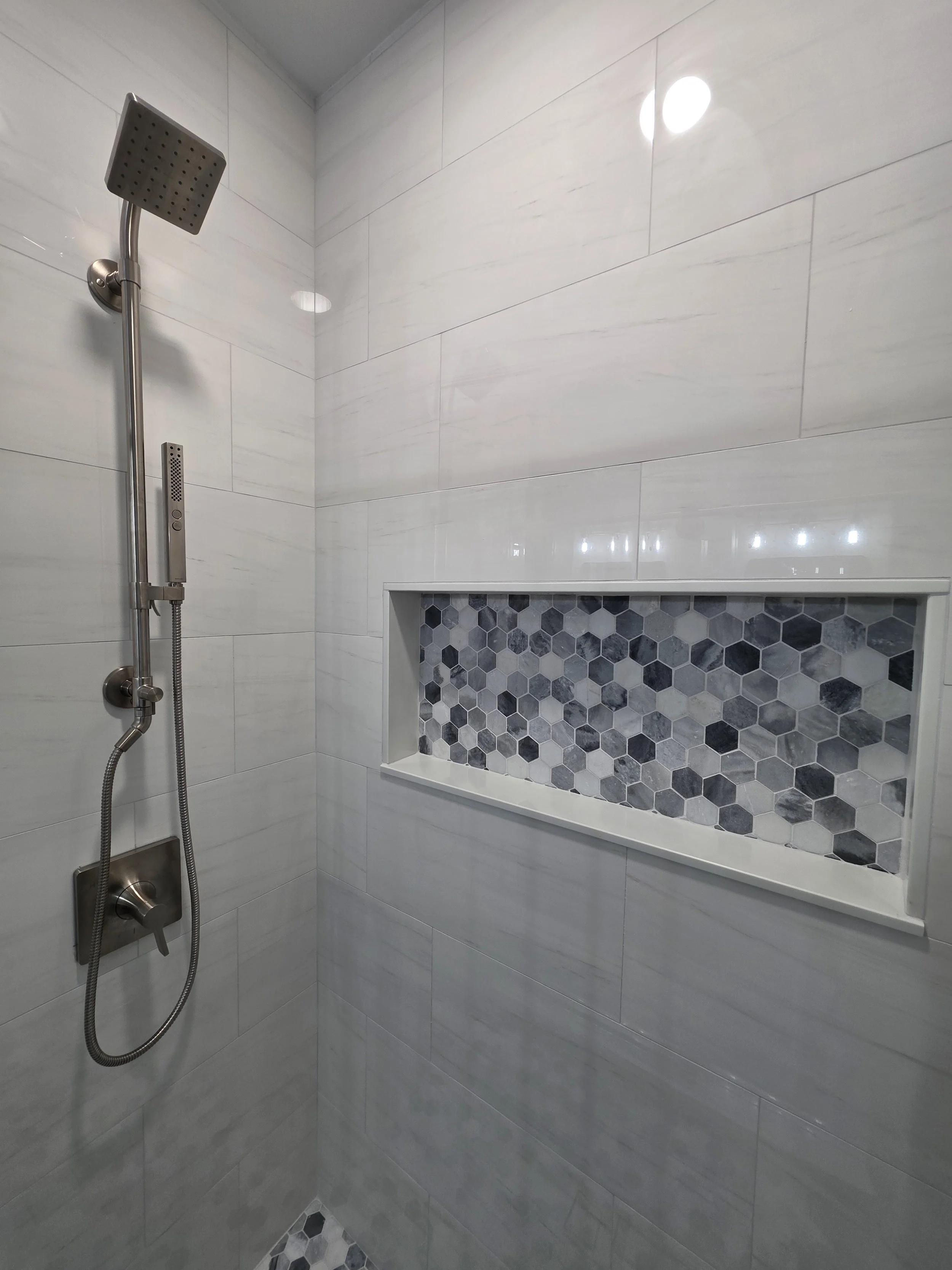 Handheld shower fixture beside mosaic-lined niche.
