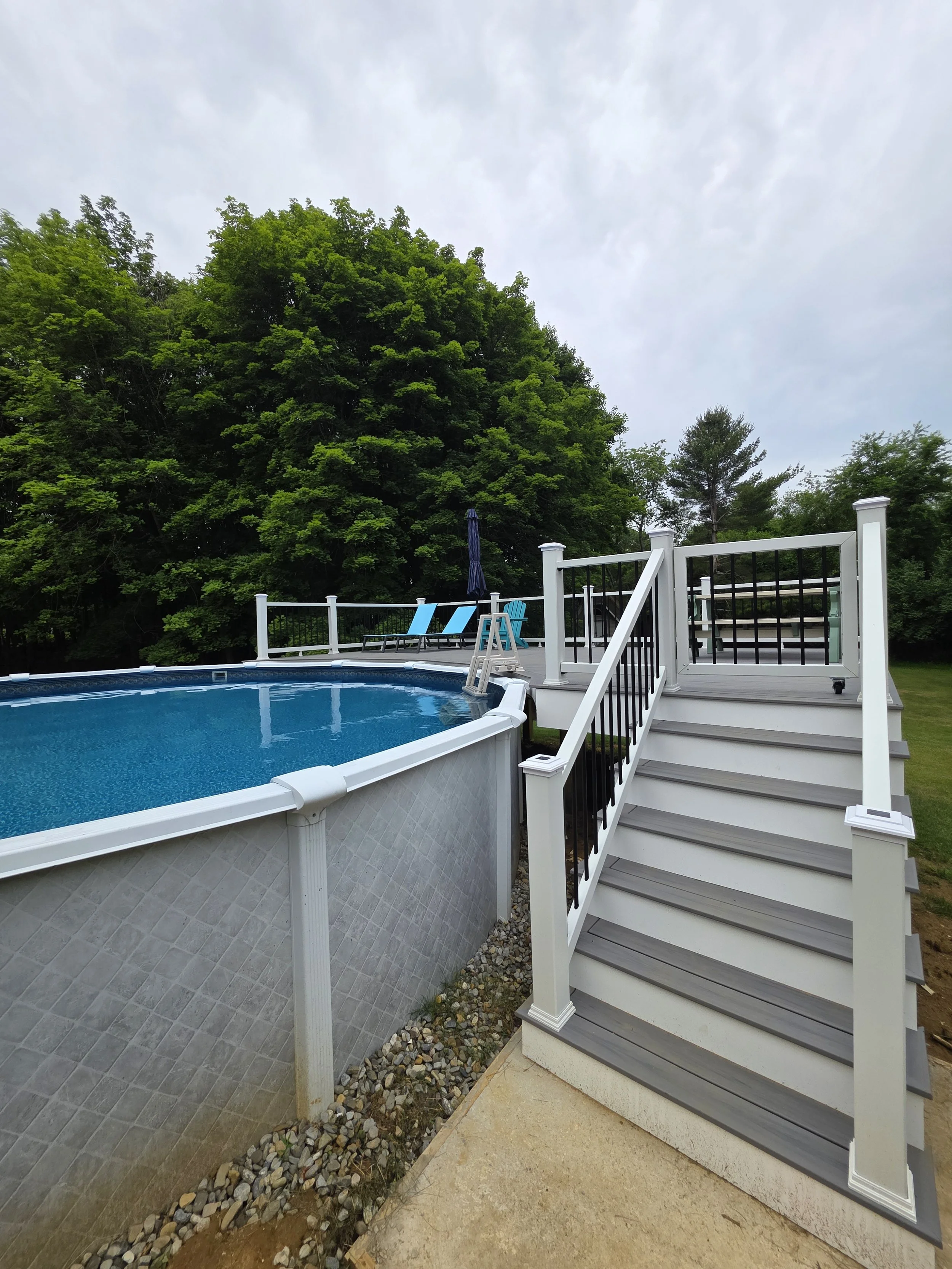 Gray stairs with white posts and dark balusters leading up to the deck beside the round above-ground pool.