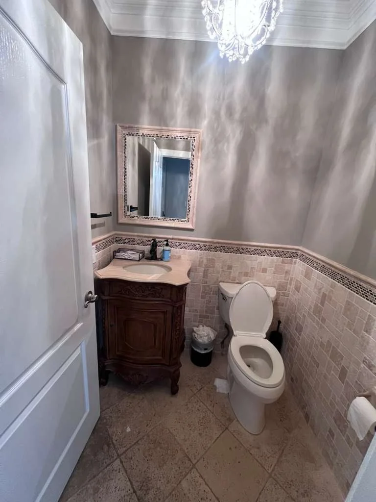 Before renovation: the original powder room with decorative wall finishes, an ornate vanity and older floor tile.