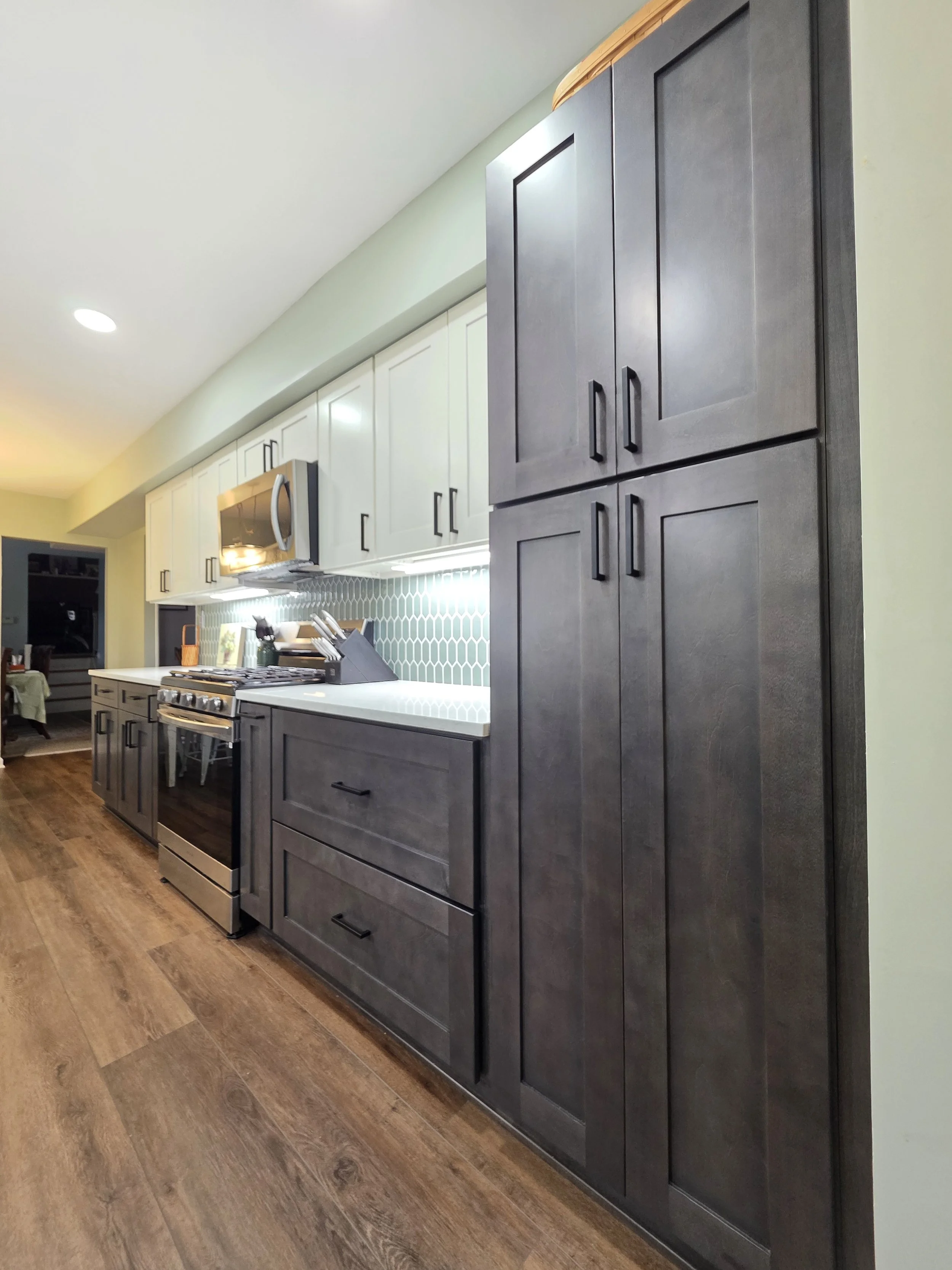 Tall dark pantry cabinet beside the range wall and continuous wood-look floor.