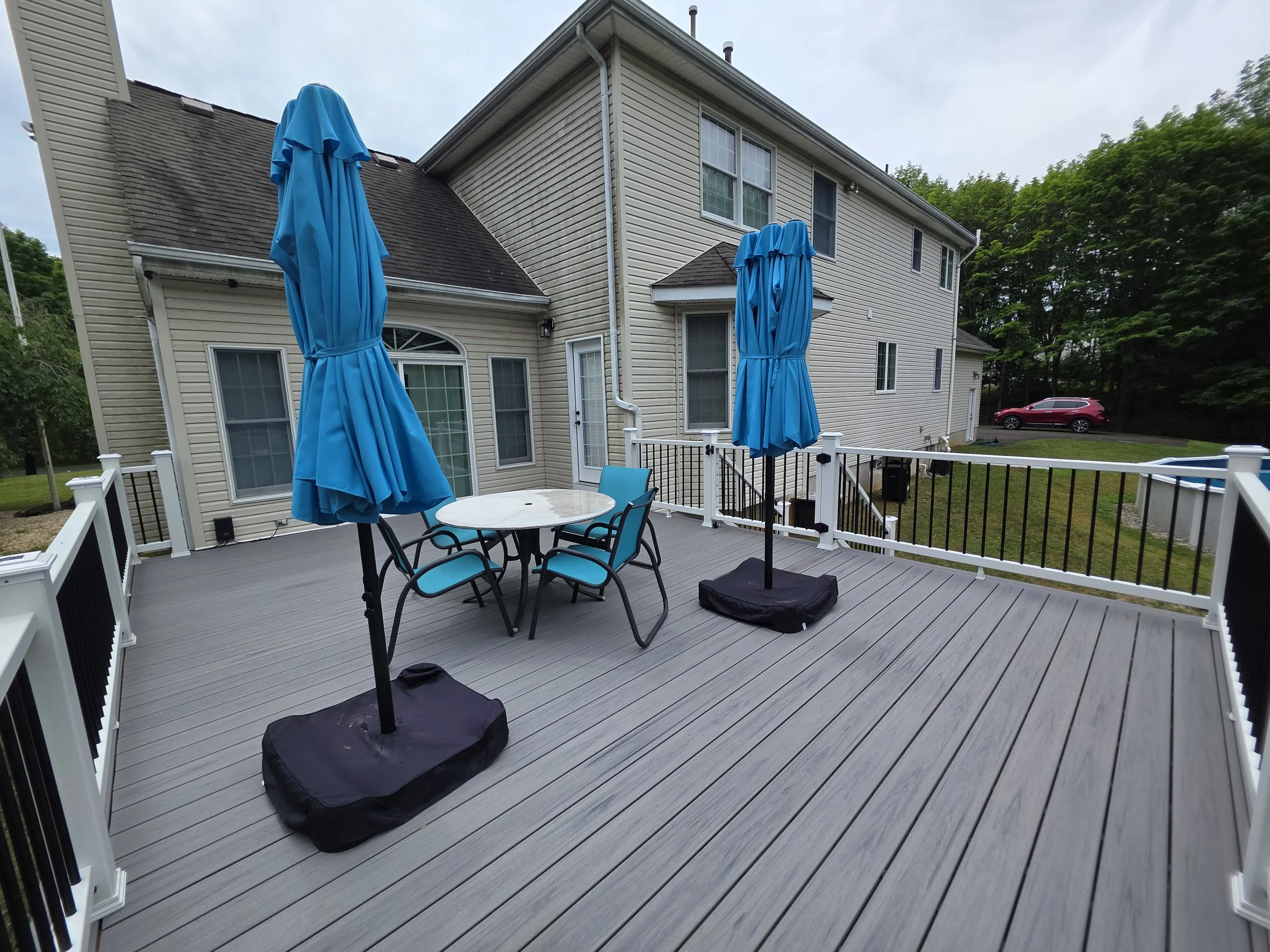 Finished attached deck looking toward the house, with gray decking, outdoor dining furniture, and white railings.
