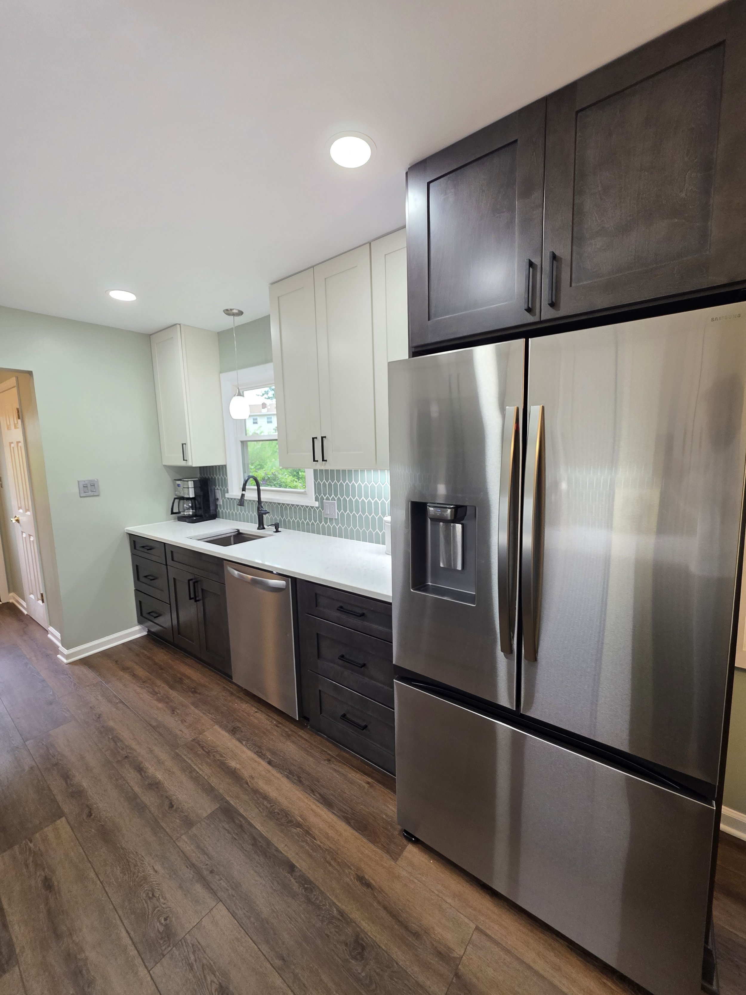 Stainless refrigerator beside dark base cabinets and a light countertop.