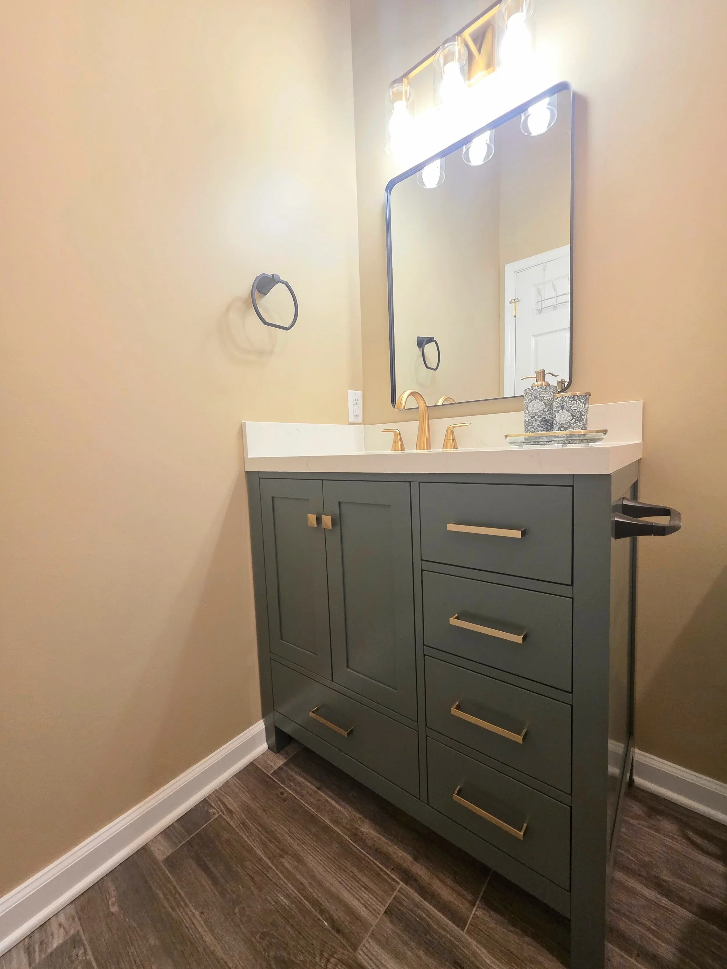 Green vanity with gold-tone hardware and faucet beneath a rectangular mirror and vanity light.