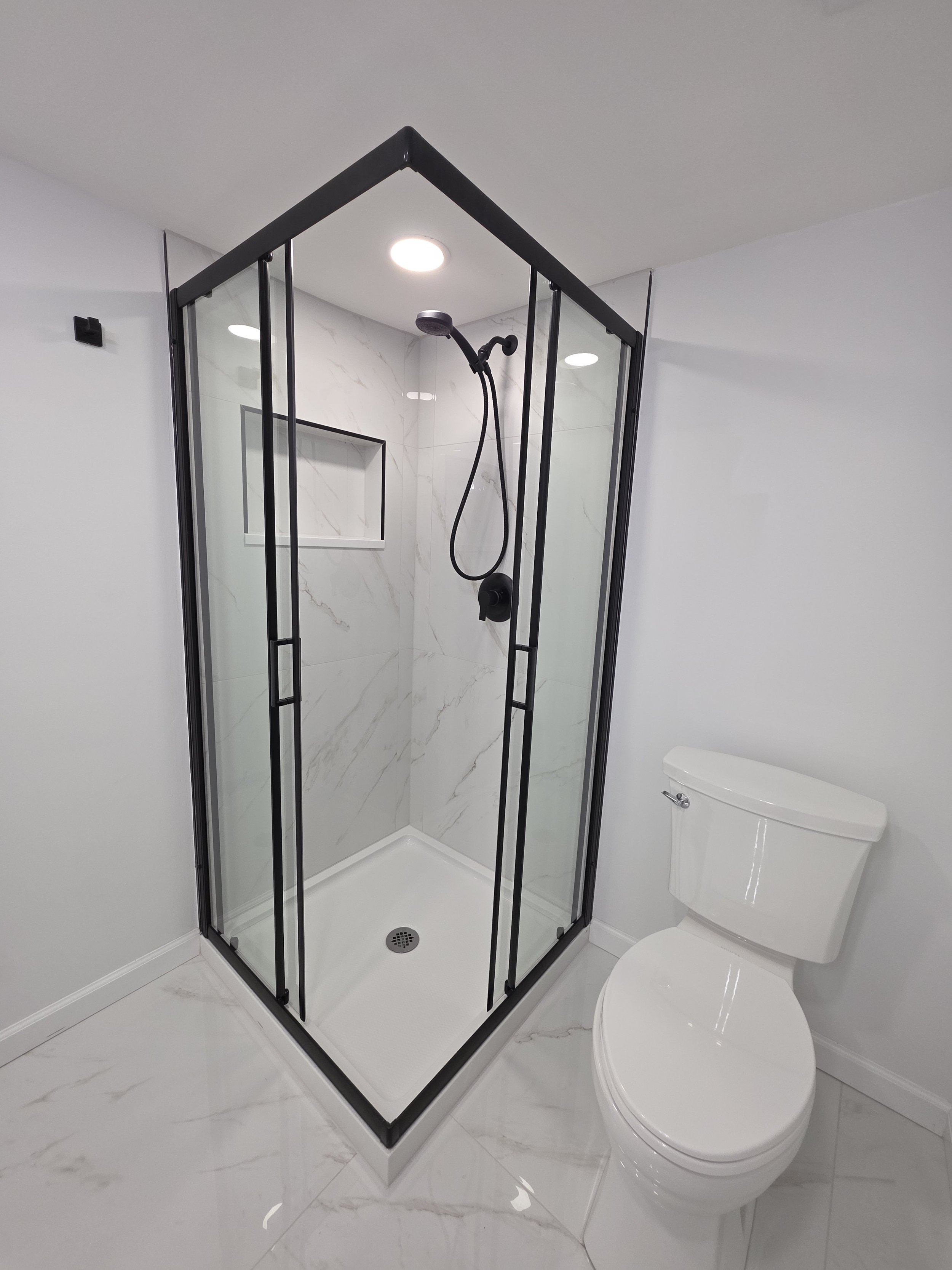 Closer view of the black-framed shower enclosure and white toilet in the basement bathroom.