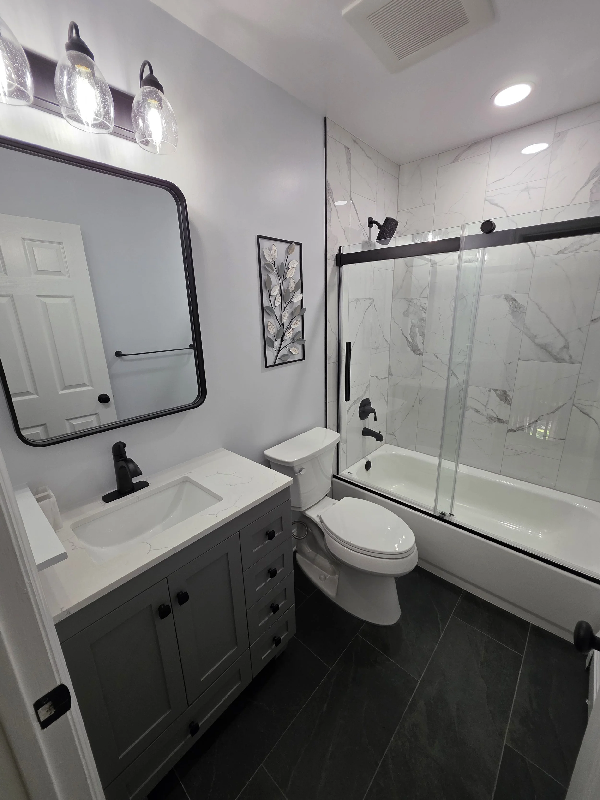 Wide view of the gray vanity, toilet and marble-look tub surround in Liz’s hallway bathroom.