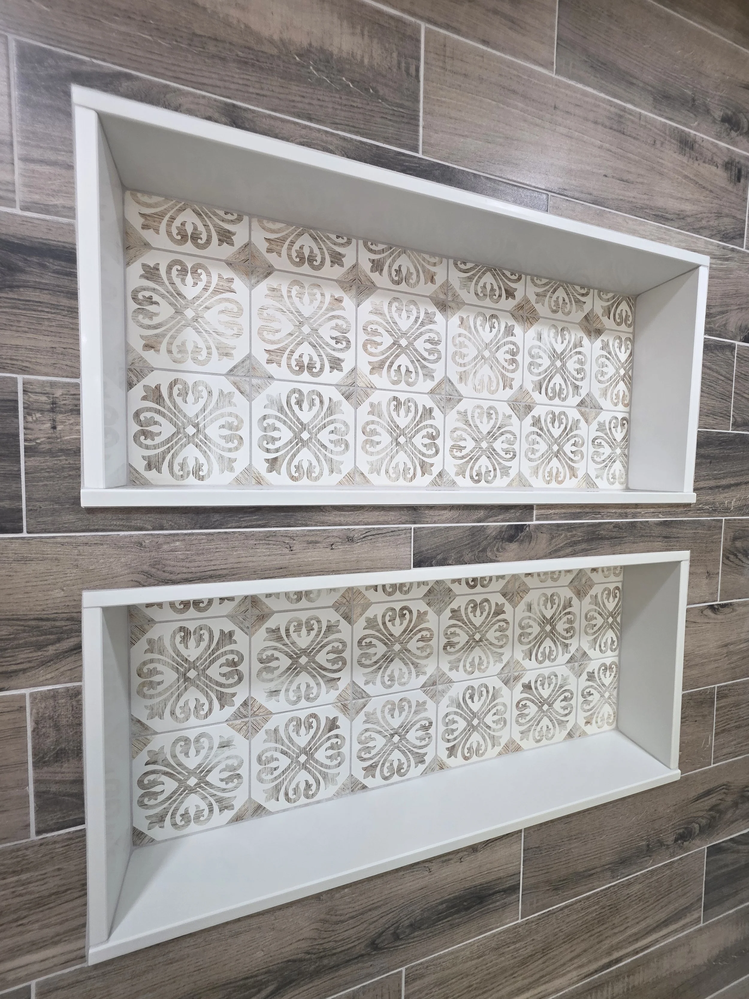 Close view of the two white-trimmed shower niches with decorative patterned tile.