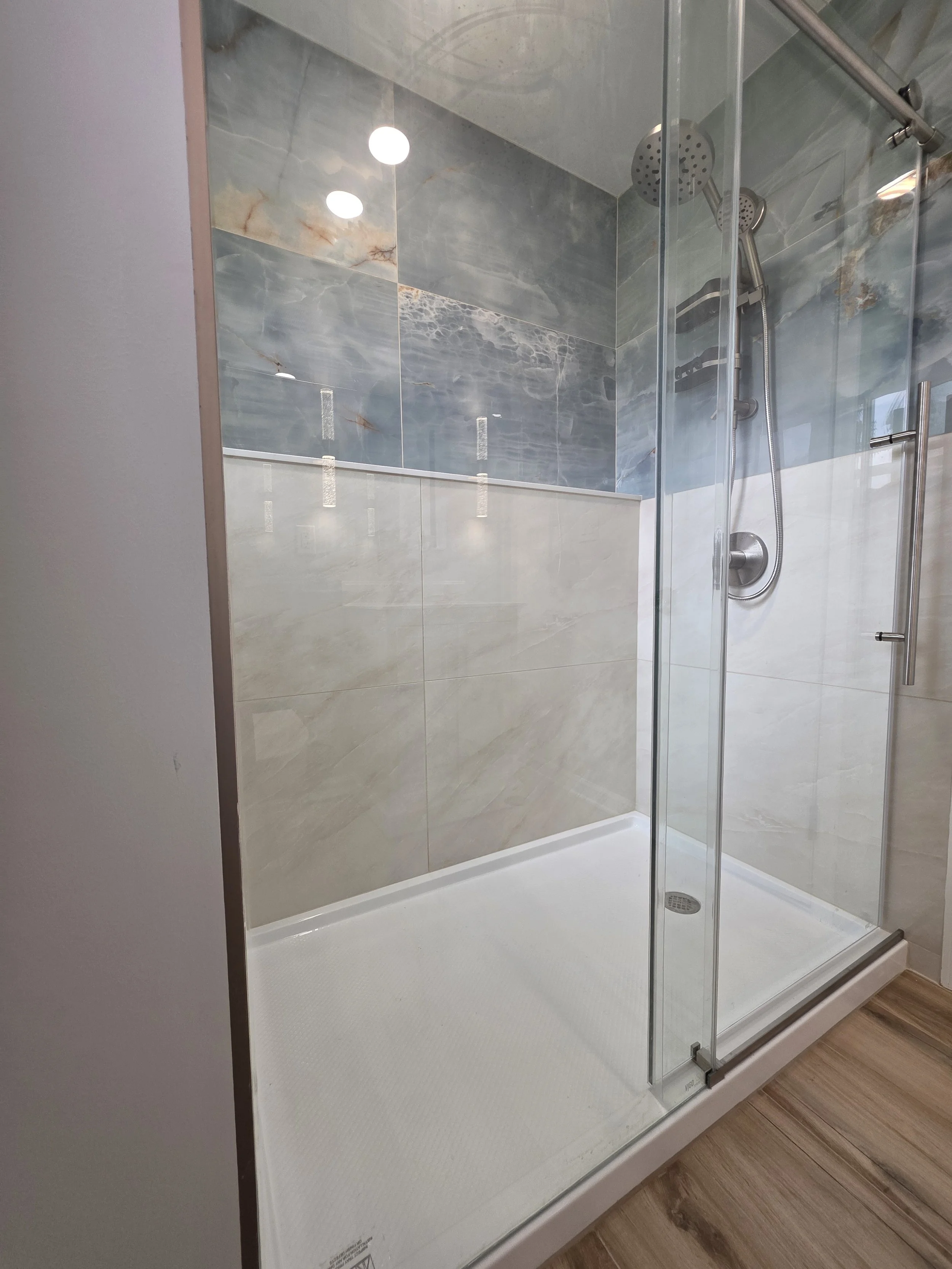 Bevin and TJ’s first-floor shower with blue and beige tile behind glass doors.