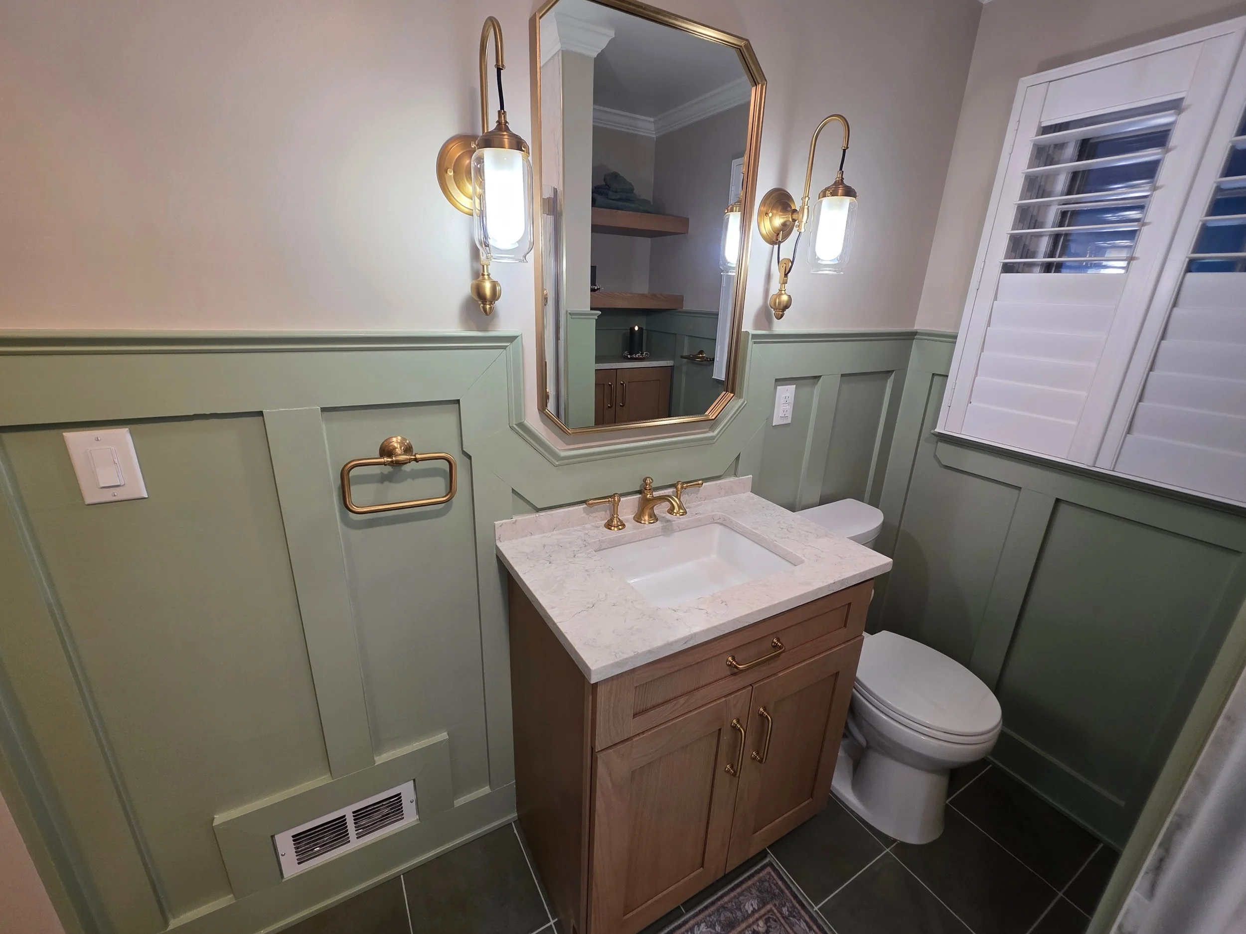 Wood vanity with gold-toned faucet and green wall paneling.