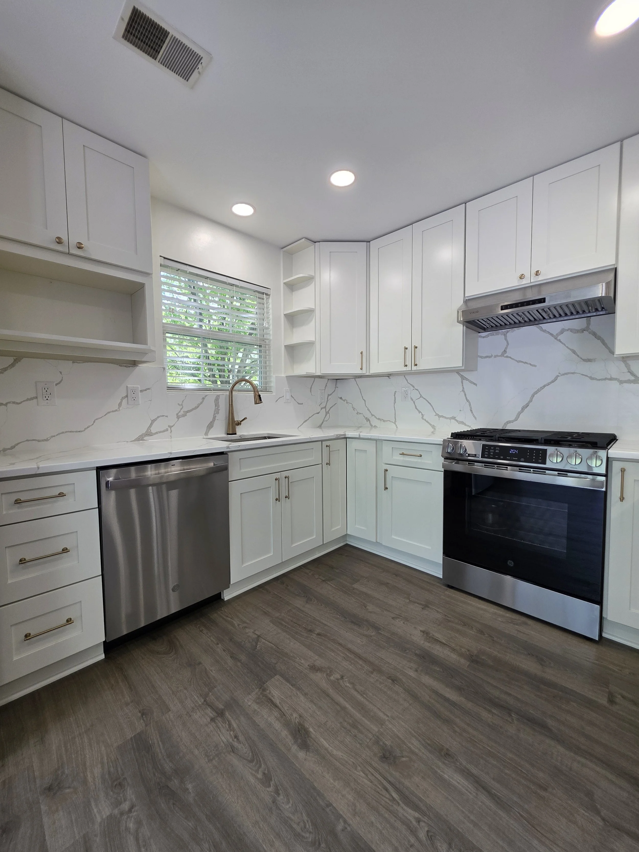 Corner view of the sink and range with white cabinetry and a continuous veined backsplash.