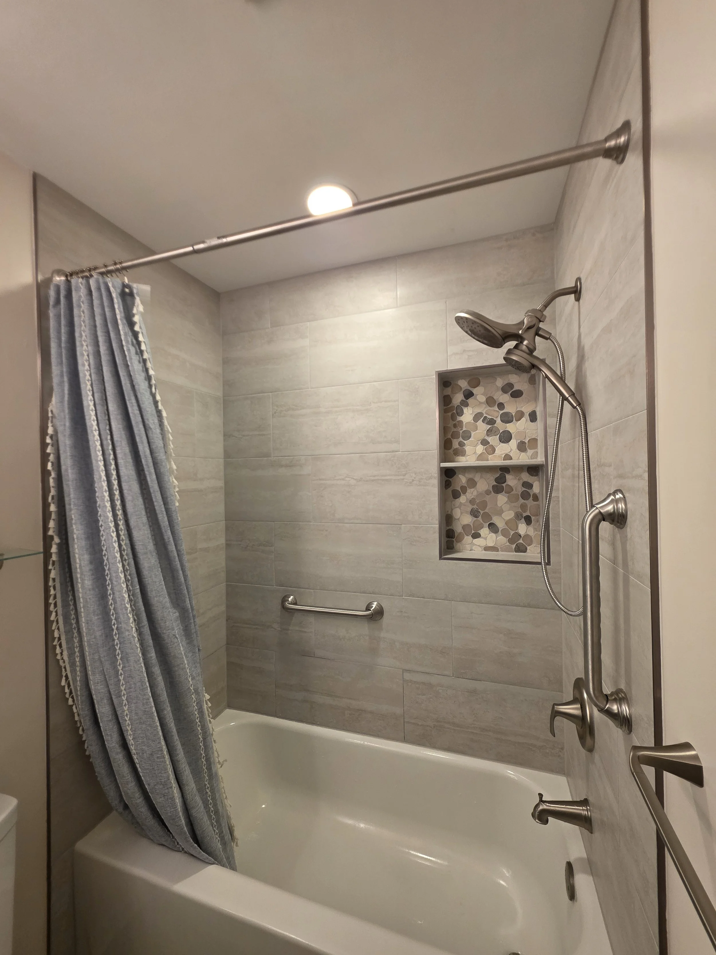 White bathtub with tiled walls, a recessed niche, handheld shower and grab bars.