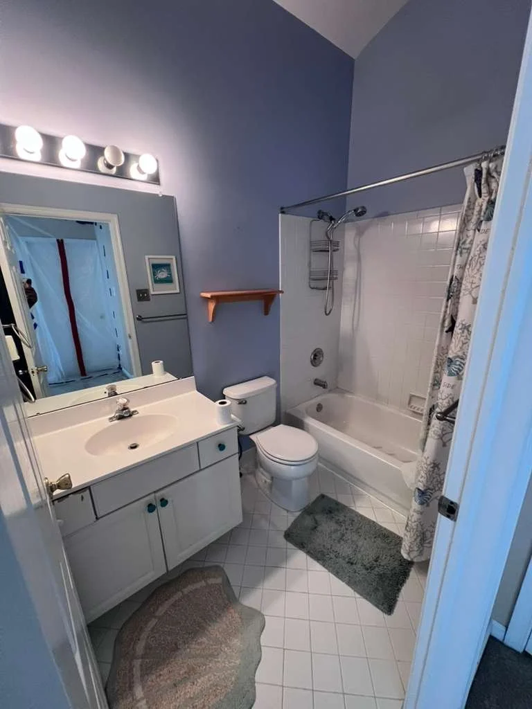Before renovation: the original bathroom with blue walls, older vanity, square floor tile and a shower curtain.
