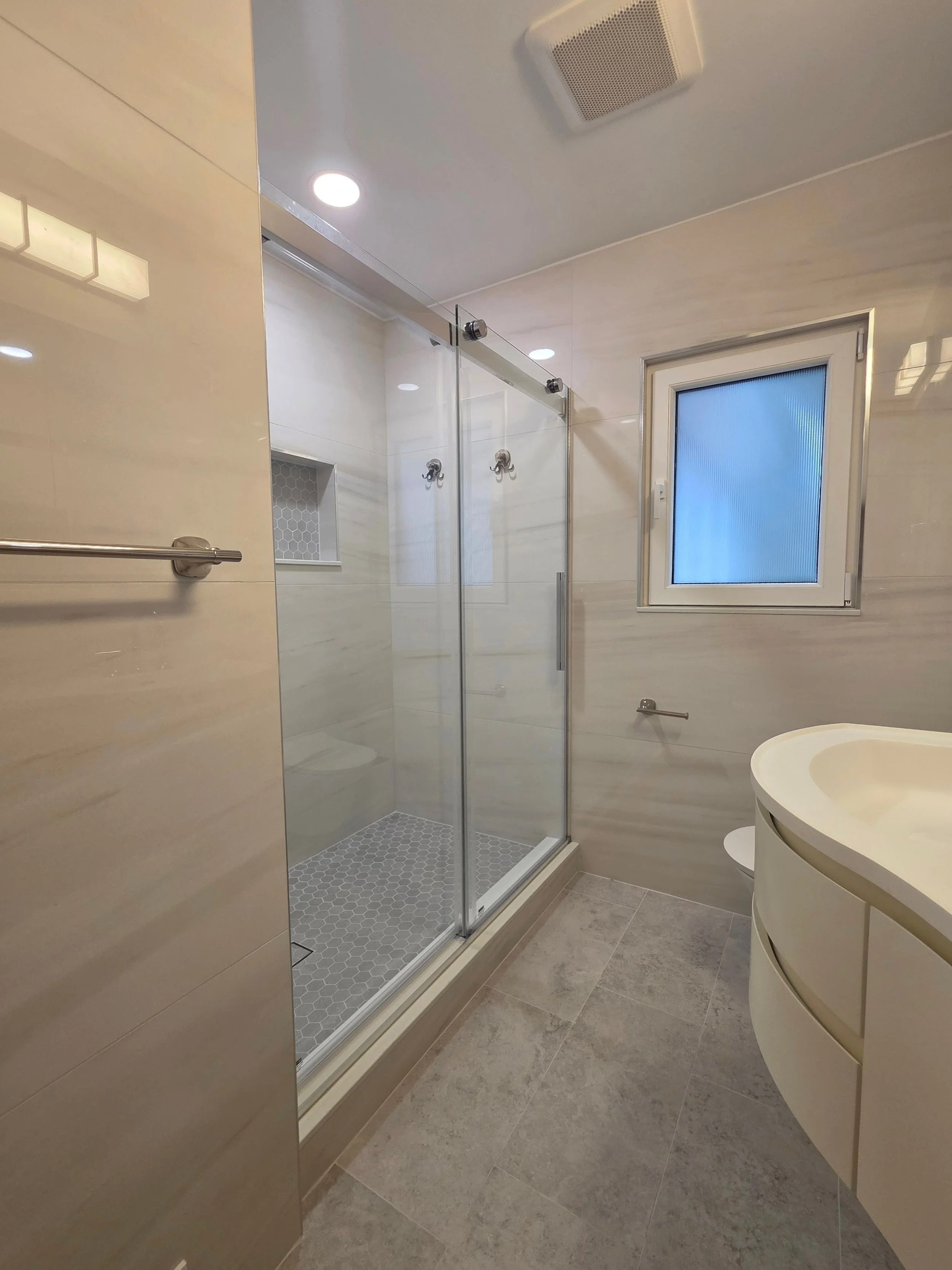 Travis’s hallway bathroom with glass shower and floating vanity.