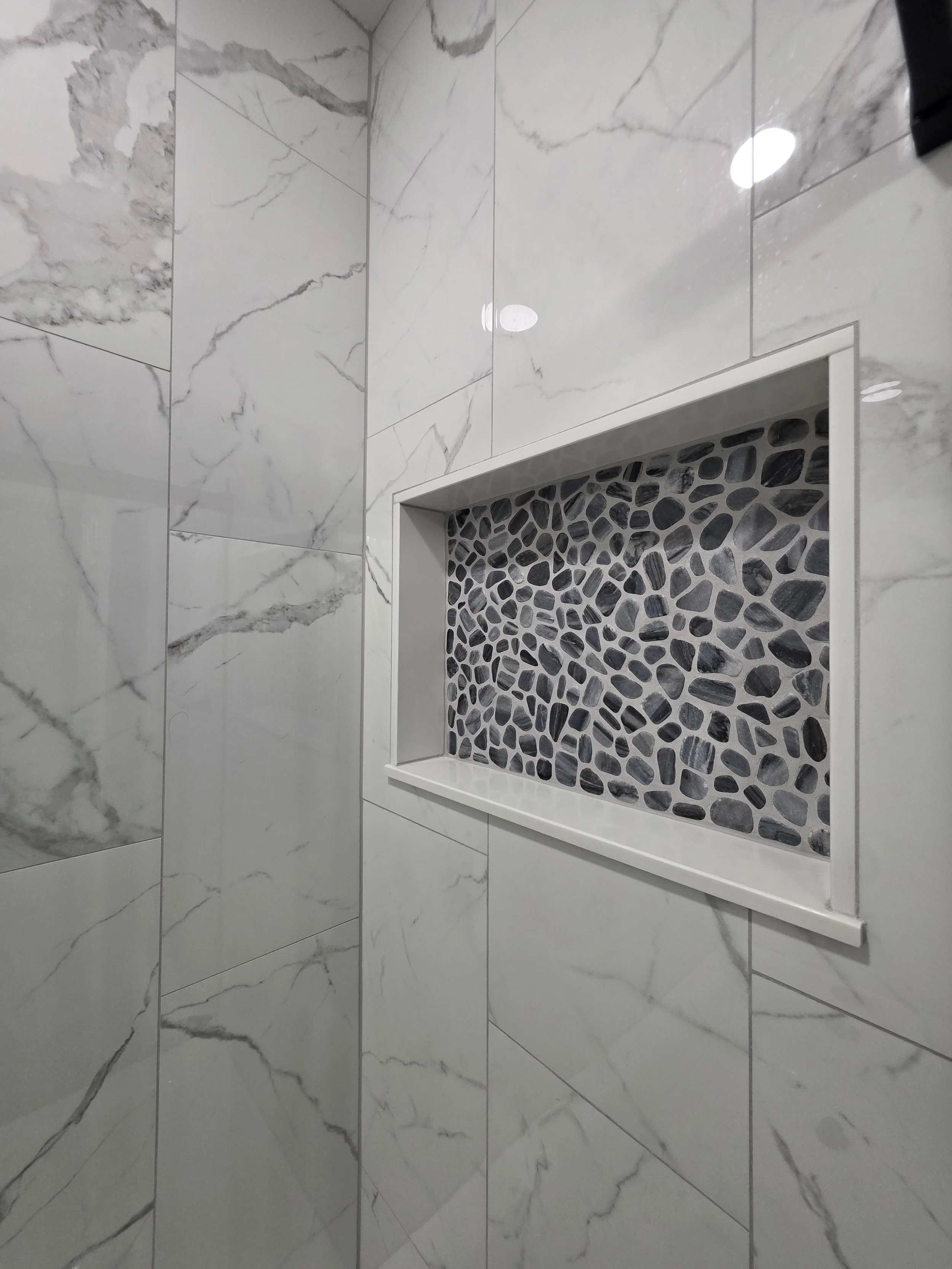 Close view of the white-trimmed recessed niche with dark pebble-pattern accent tile.
