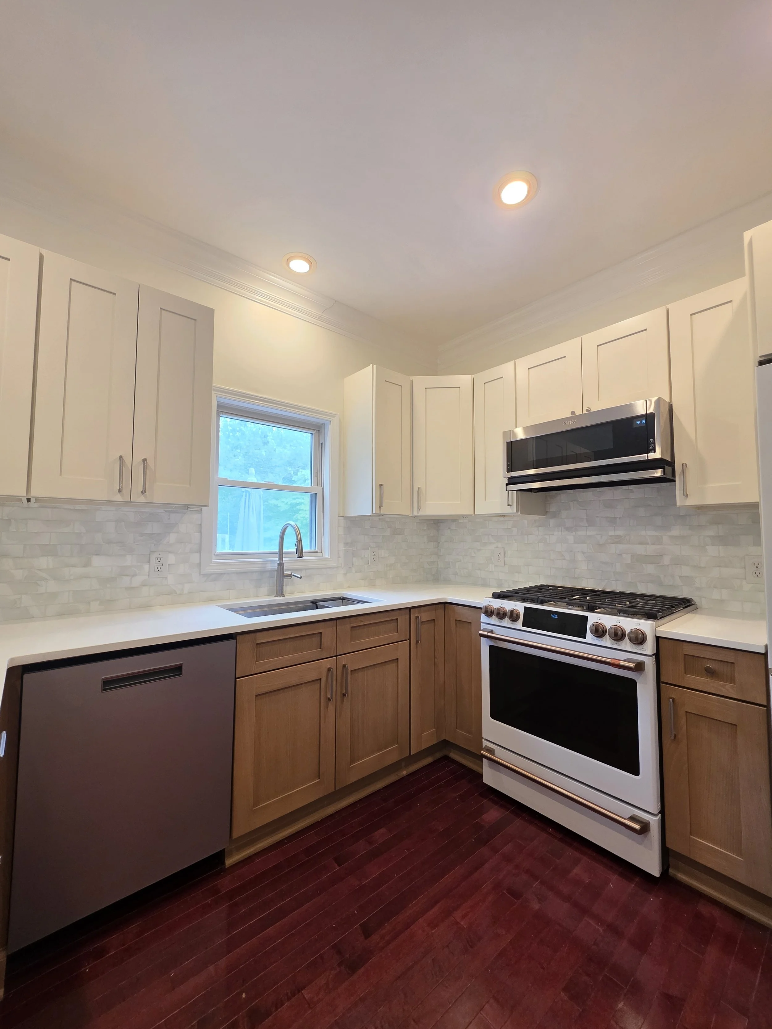 Corner view of the updated kitchen showing the sink, range, white upper cabinets, and wood-tone lower cabinets.