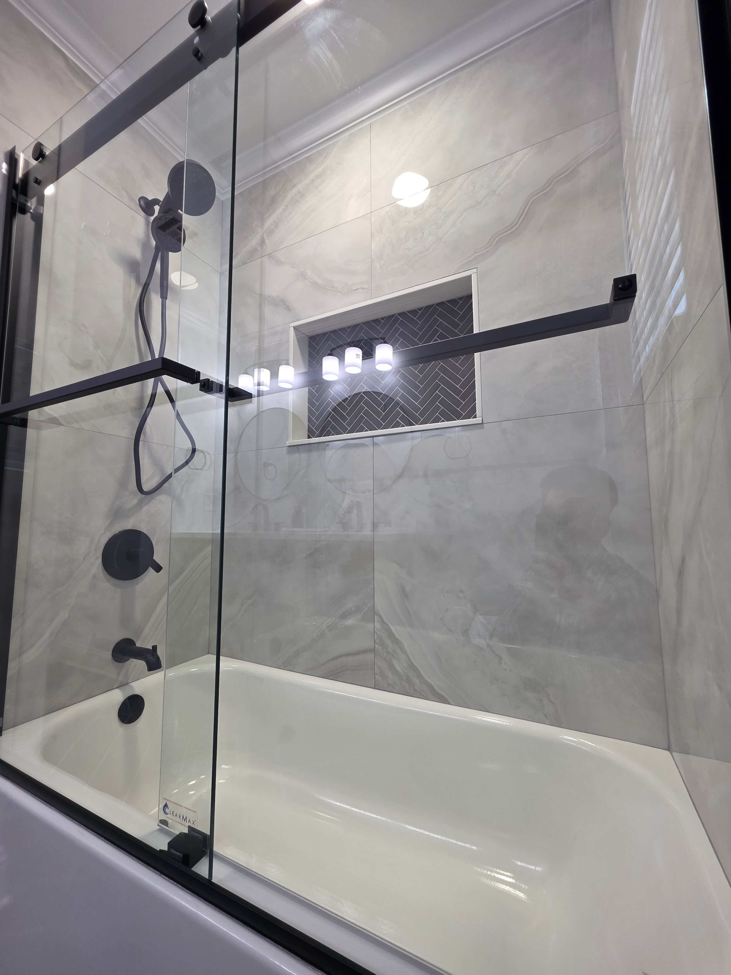 Glass tub enclosure with black sliding-door hardware, black shower fixtures and a wide recessed niche.