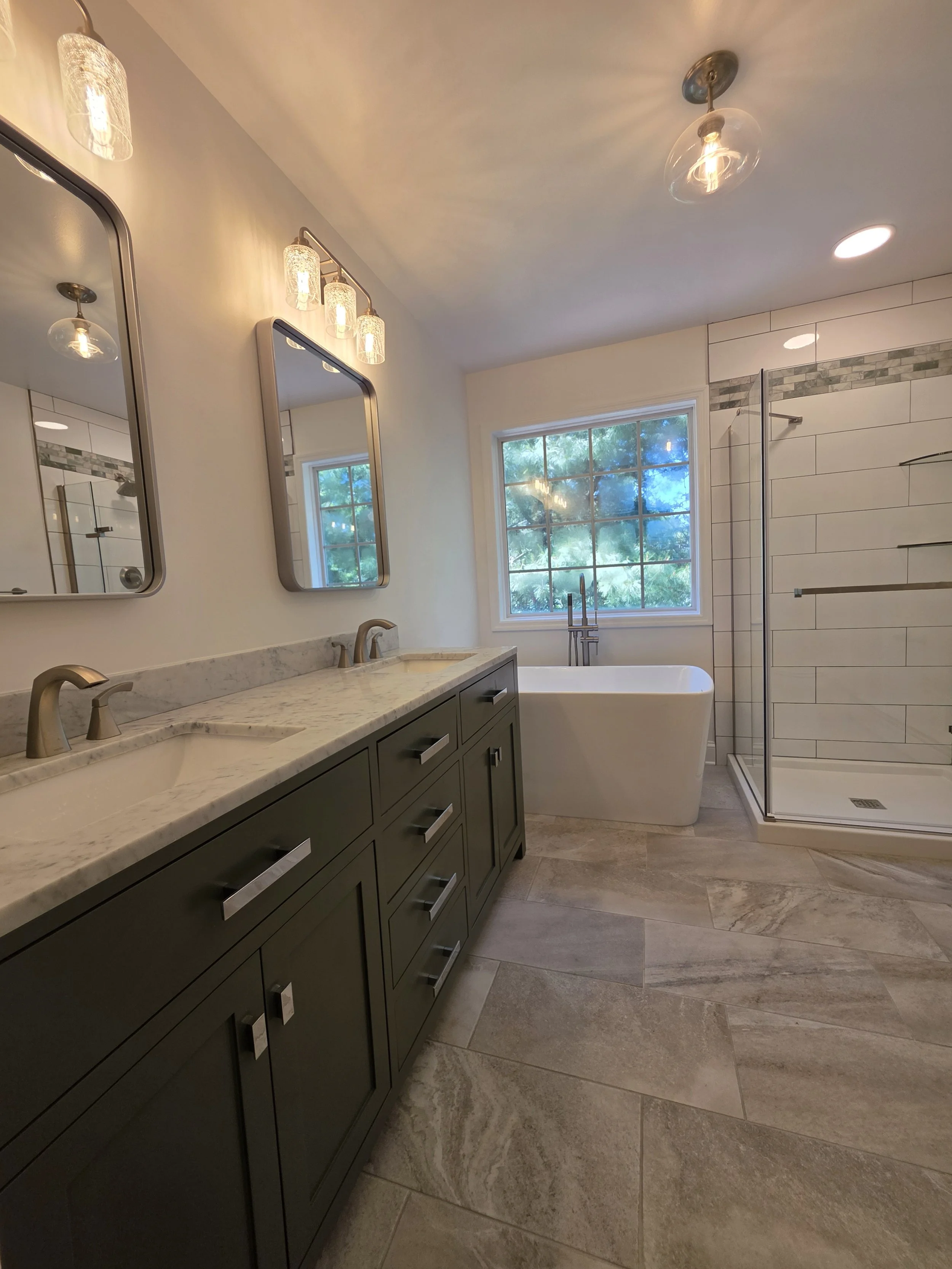 Liz’s remodeled master bathroom with a green double vanity, freestanding tub, glass shower and patterned floor tile.