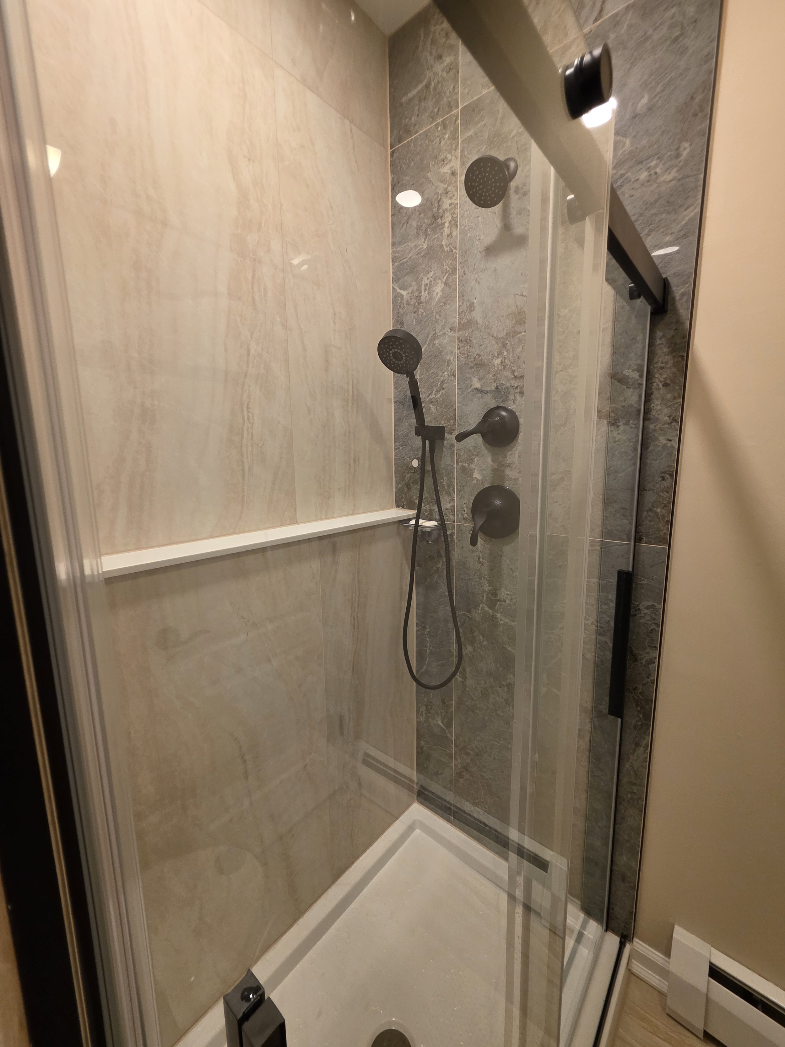 Glass shower enclosure with neutral wall tile, a contrasting shower-fixture wall and black hardware.