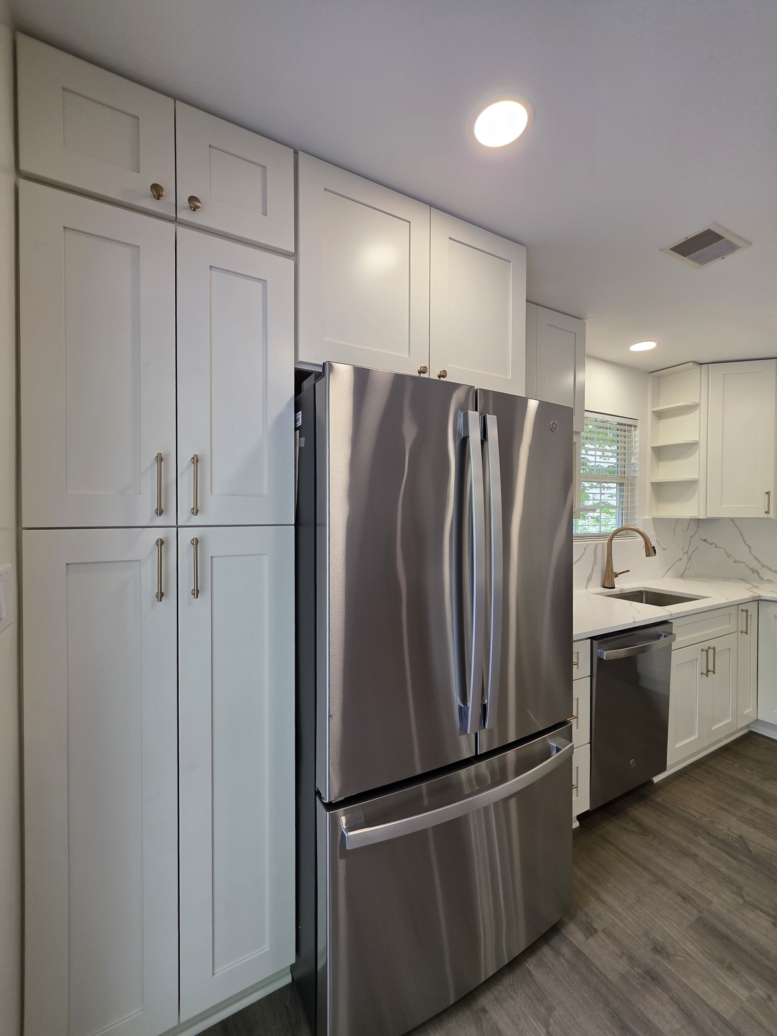 Tall pantry cabinets surrounding the stainless refrigerator beside the kitchen sink.