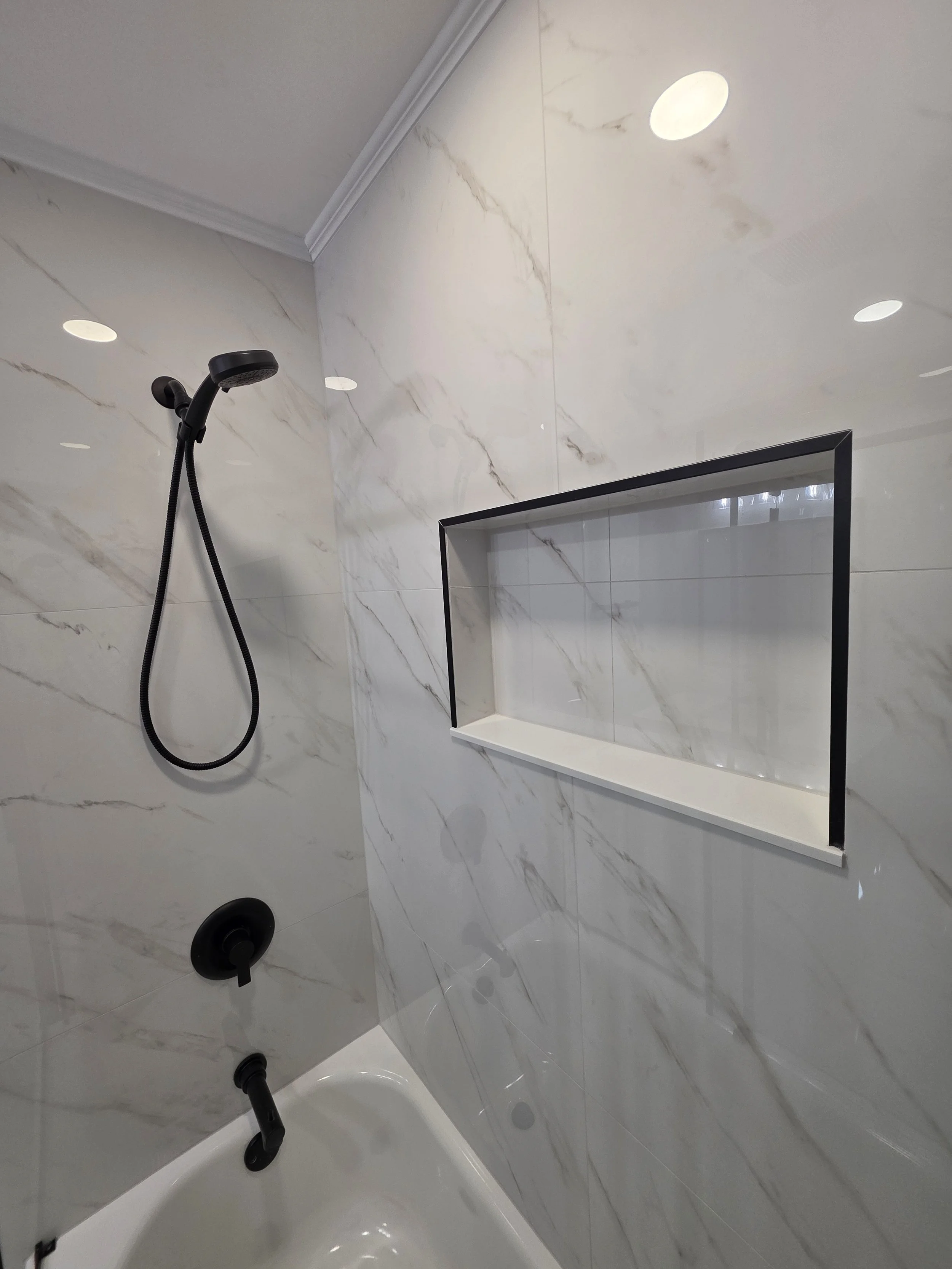 Handheld shower, black tub spout and recessed niche above the white bathtub.