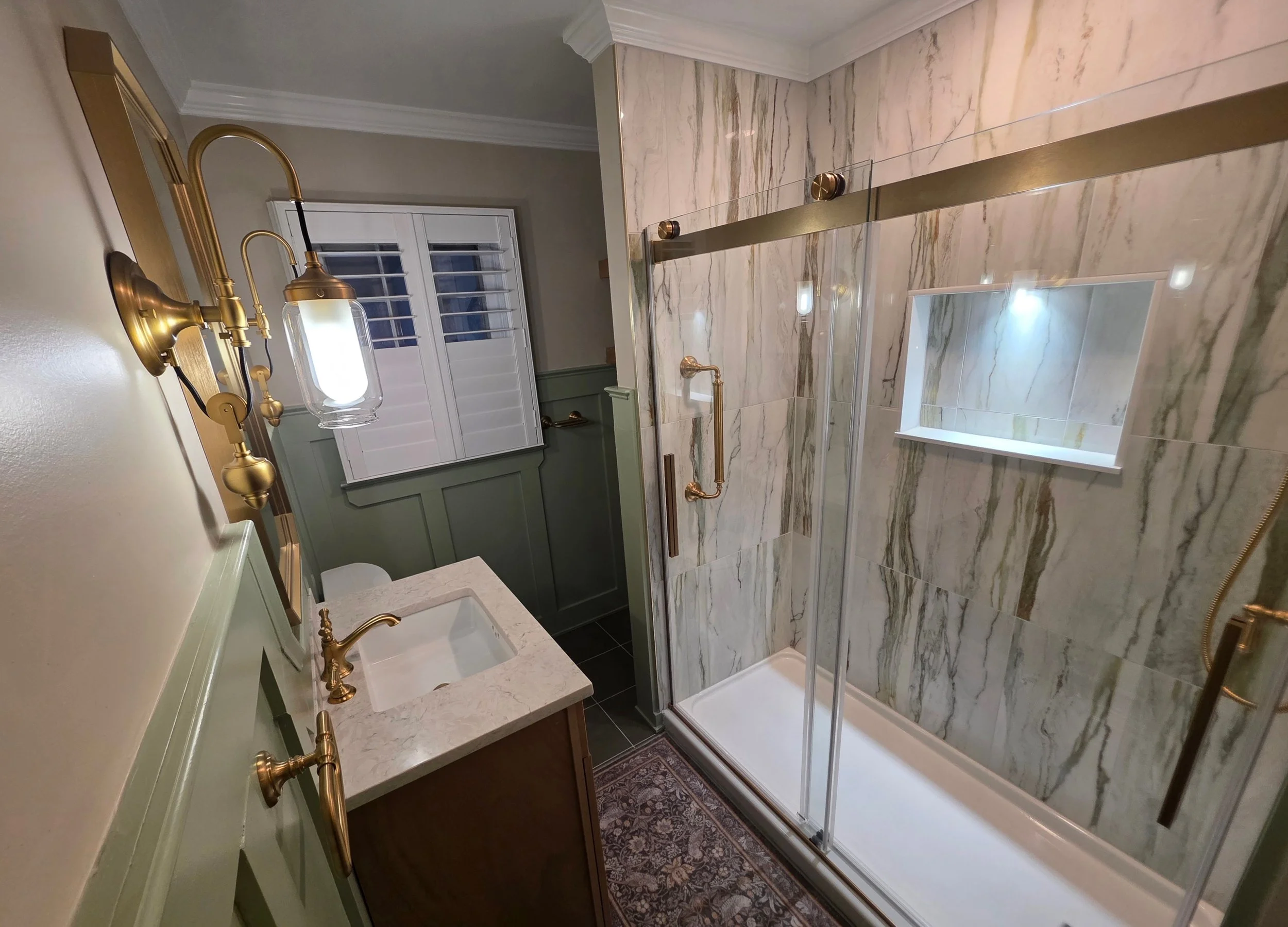 Heather’s hallway bathroom with green paneling, wood vanity and glass shower.