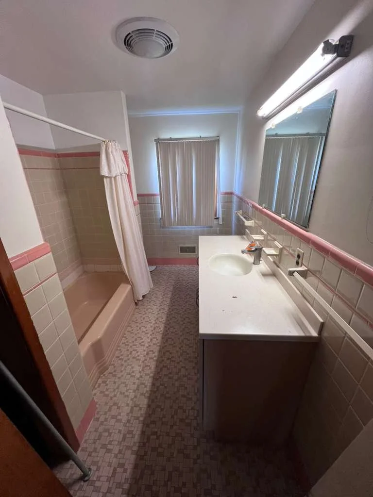 Hallway bathroom before renovation with older vanity and tub.