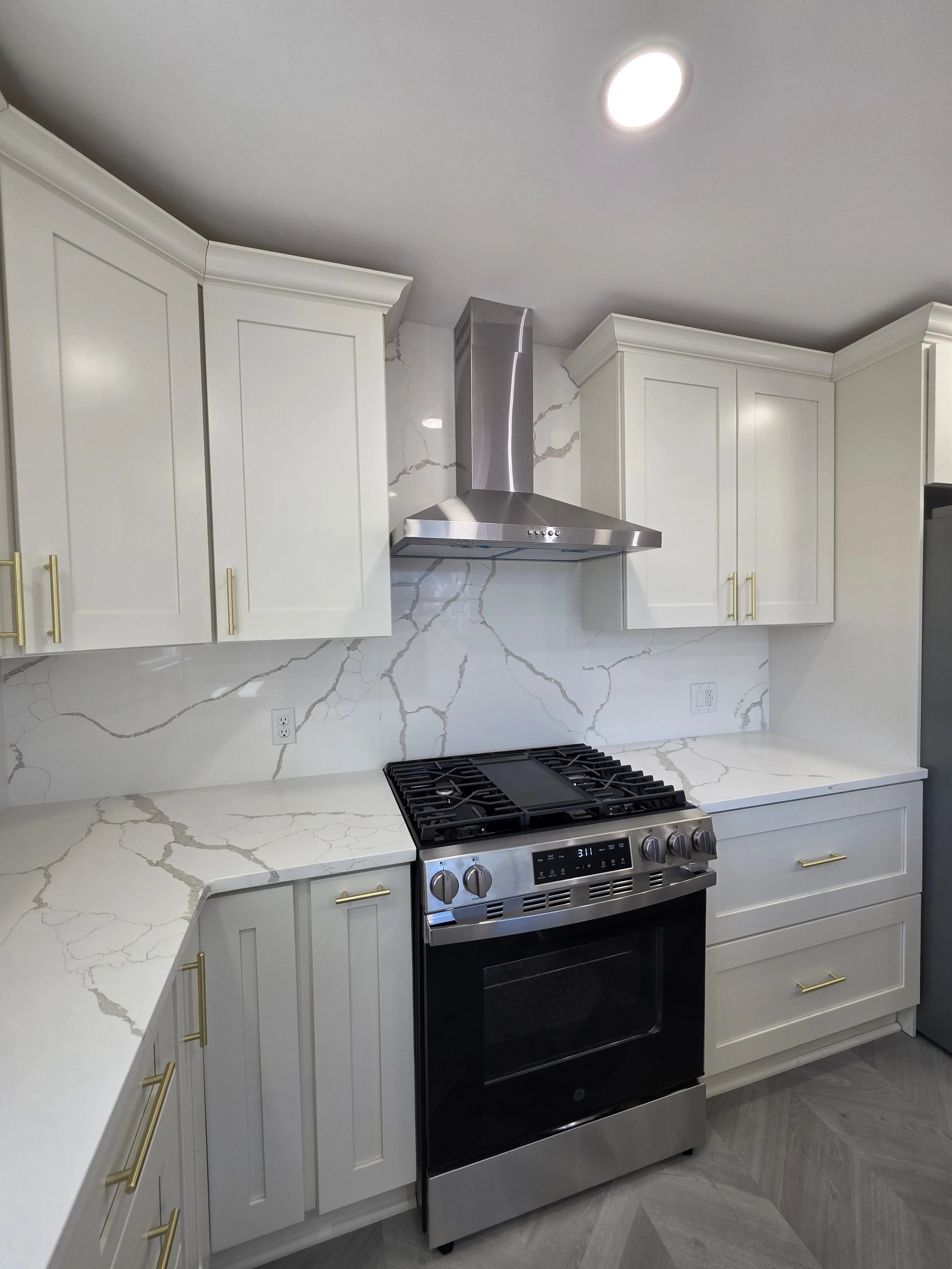 Wide view of the range wall, white cabinetry and herringbone-pattern floor.